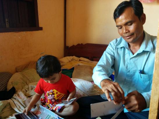 Journalist Sa Piseth at home with his son, going through photos of illegal logs. Image by Saul Elbein. Cambodia, 2014. Journalist Sa Piseth at home with his son, going through photos of illegal logs. Image by Saul Elbein. Cambodia, 2014.