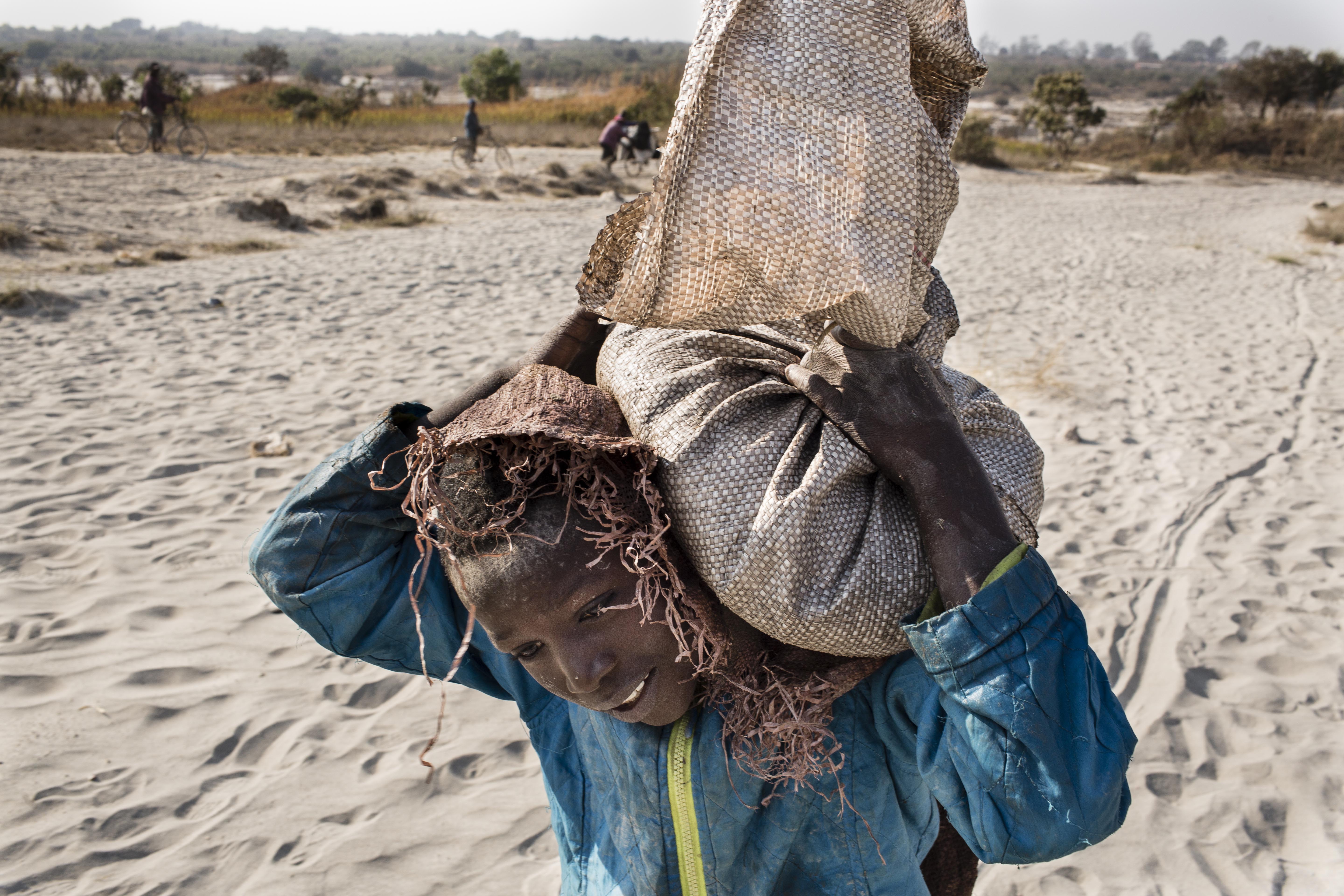 Daniel (11) carries a bag of cobalt on his back. He works in a mine ferrying sacks of cobalt to a depot. Image by Sebastian Meyer. Democratic Republic of the Congo, 2018. Daniel (11) carries a bag of cobalt on his back. He works in a mine ferrying sacks of cobalt to a depot. Image by Sebastian Meyer. Democratic Republic of the Congo, 2018.