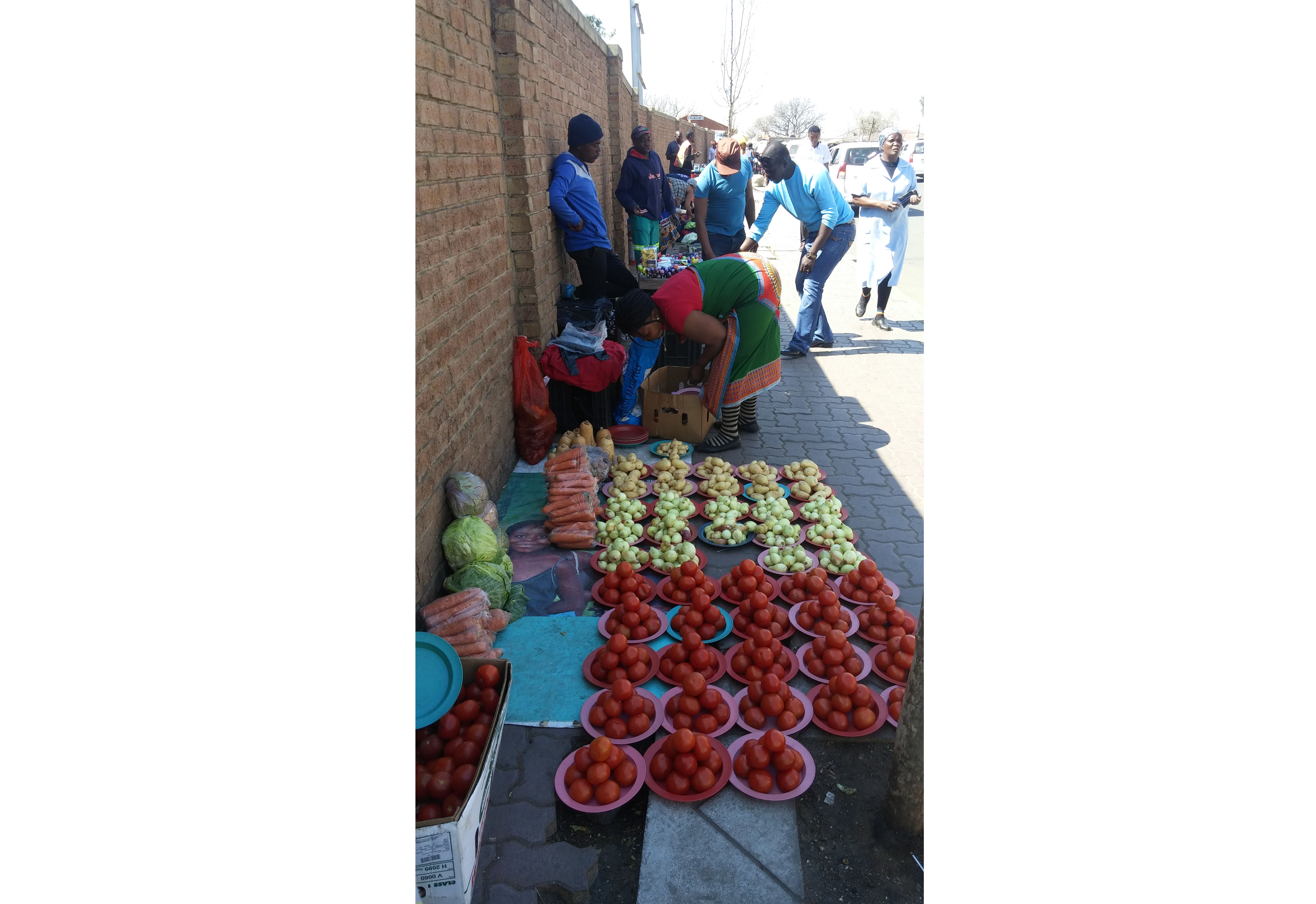 An informal trader sells produce outside of Pan Africa Shopping Centre. Vendors like this are quick sources of food for many of Alex's residents, who lack access to the refrigeration necessary to store food for extended periods of time. Image by Christian Belanger. South Africa, 2016. Media file: south_africa_cropped.jpg