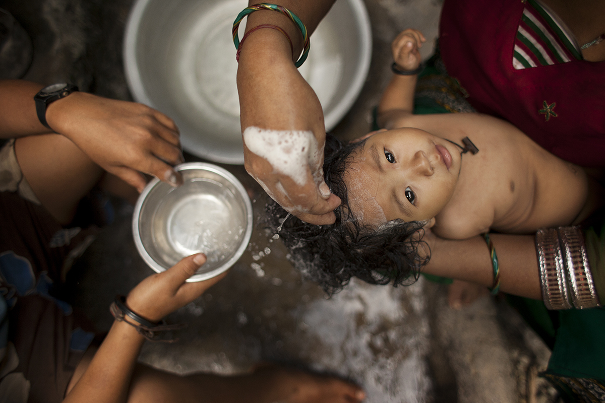 Deepika Shrestha is bathed in the streets by her mother in the village of Barah Chhetra. Image by Steve Matzker. Nepal, 2013.