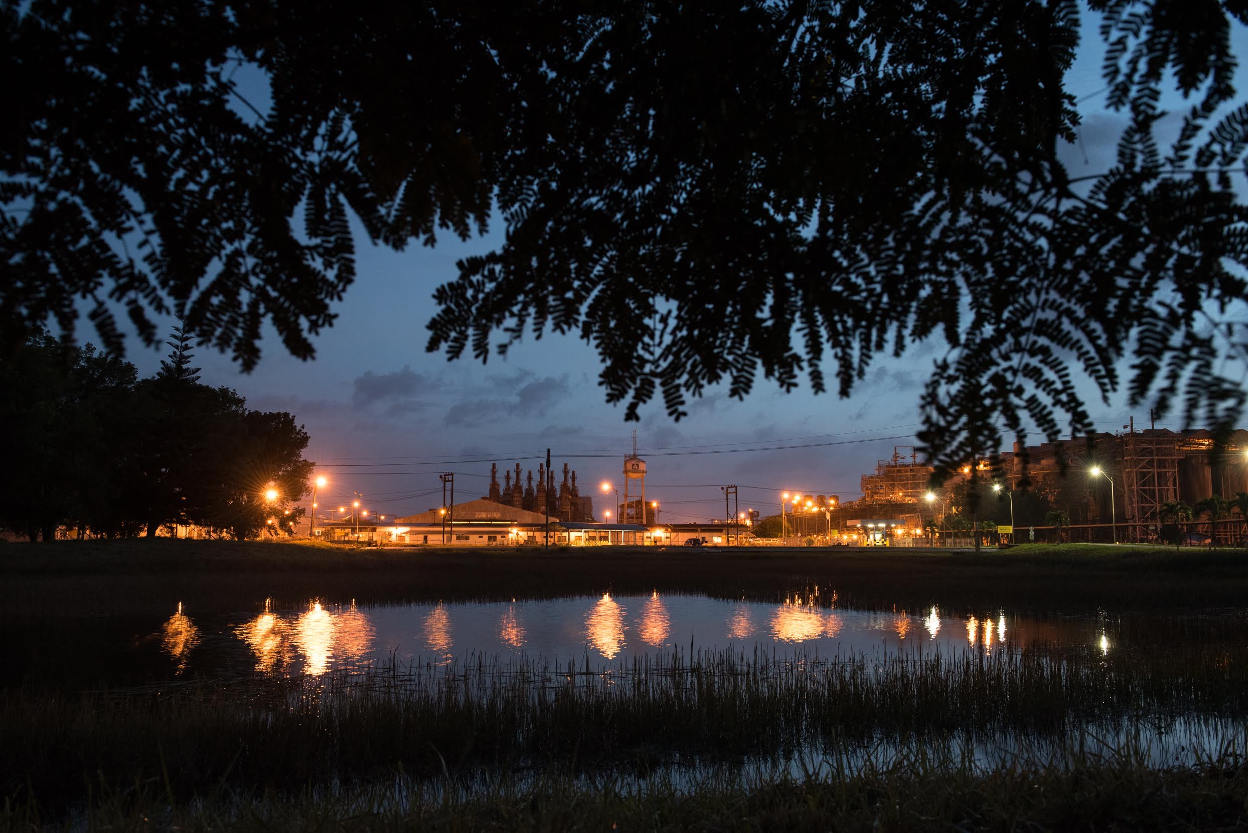 The sky at dusk is cut by the orange glow of the refinery at the Paranam Operations for Suralco, a subsidiary of Alcoa. The plant is no longer operational. Image by Stephanie Strasburg/Pittsburgh Post-Gazette. Suriname, 2017. The sky at dusk is cut by the orange glow of the refinery at the Paranam Operations for Suralco, a subsidiary of Alcoa. The plant is no longer operational. Image by Stephanie Strasburg/Pittsburgh Post-Gazette. Suriname, 2017.
