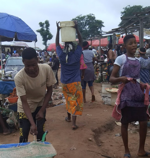 A woman carries a bucket of water on her head at Gosa market. Image by Anita Igbine. Nigeria, 2020. A woman carries a bucket of water on her head at Gosa market. Image by Anita Igbine. Nigeria, 2020.