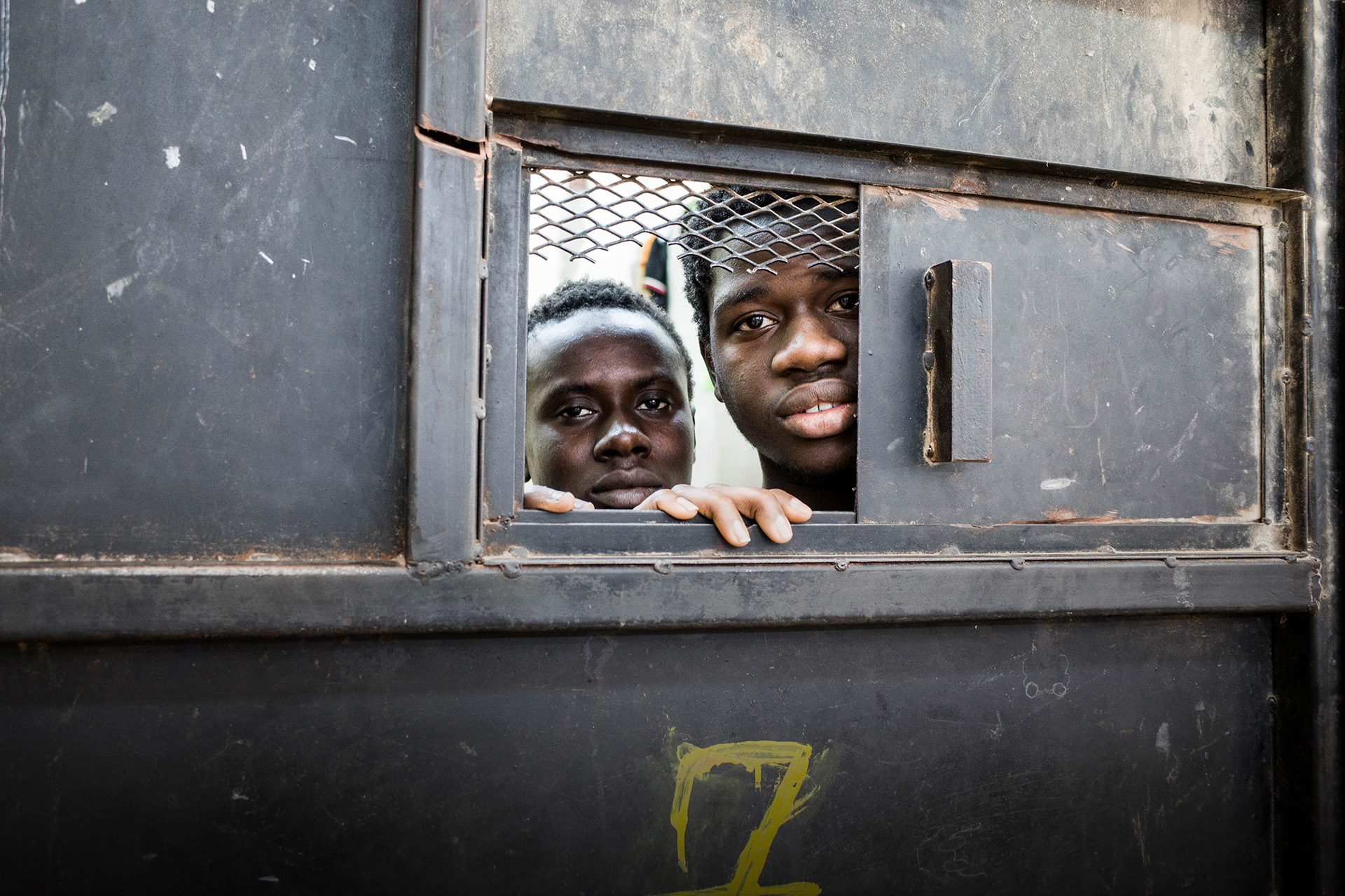 Detainees from West Africa peer out of their overcrowded cell in the al-Nasr detention center in Zawiya, Libya, where migrants intercepted by the Coast Guard in Zawiya are warehoused indefinitely. Image by Peter Tinti. Libya, 2017. Detainees from West Africa peer out of their overcrowded cell in the al-Nasr detention center in Zawiya, Libya, where migrants intercepted by the Coast Guard in Zawiya are warehoused indefinitely. Image by Peter Tinti. Libya, 2017.