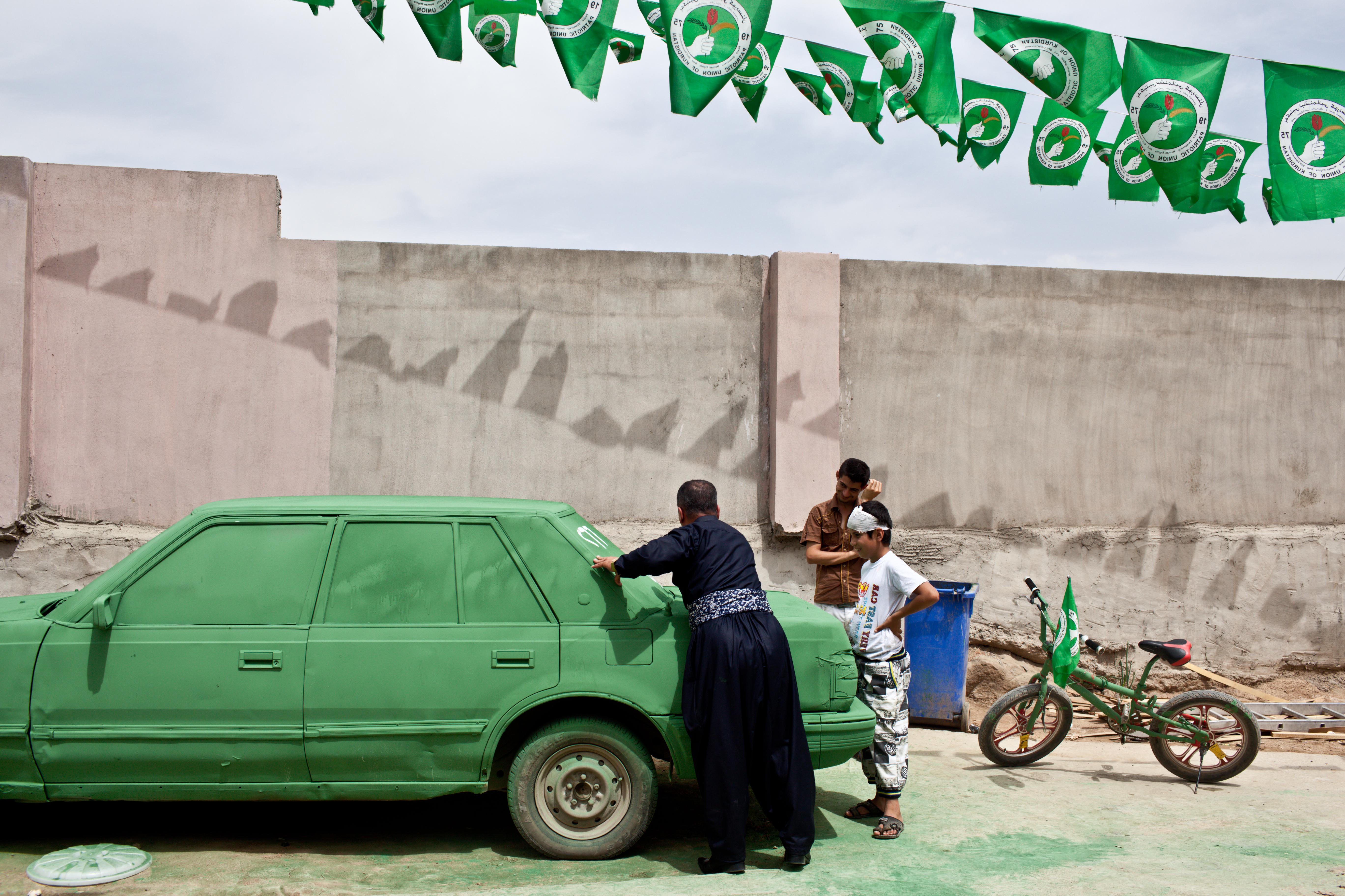 A supporter of the Patriotic Union of Kurdistan (PUK), a Kurdish political party headed by Jalal Talabani, paints slogans on a car which was painted green, the color of the party. Image by Sebastian Meyer. Iraq, 2014.