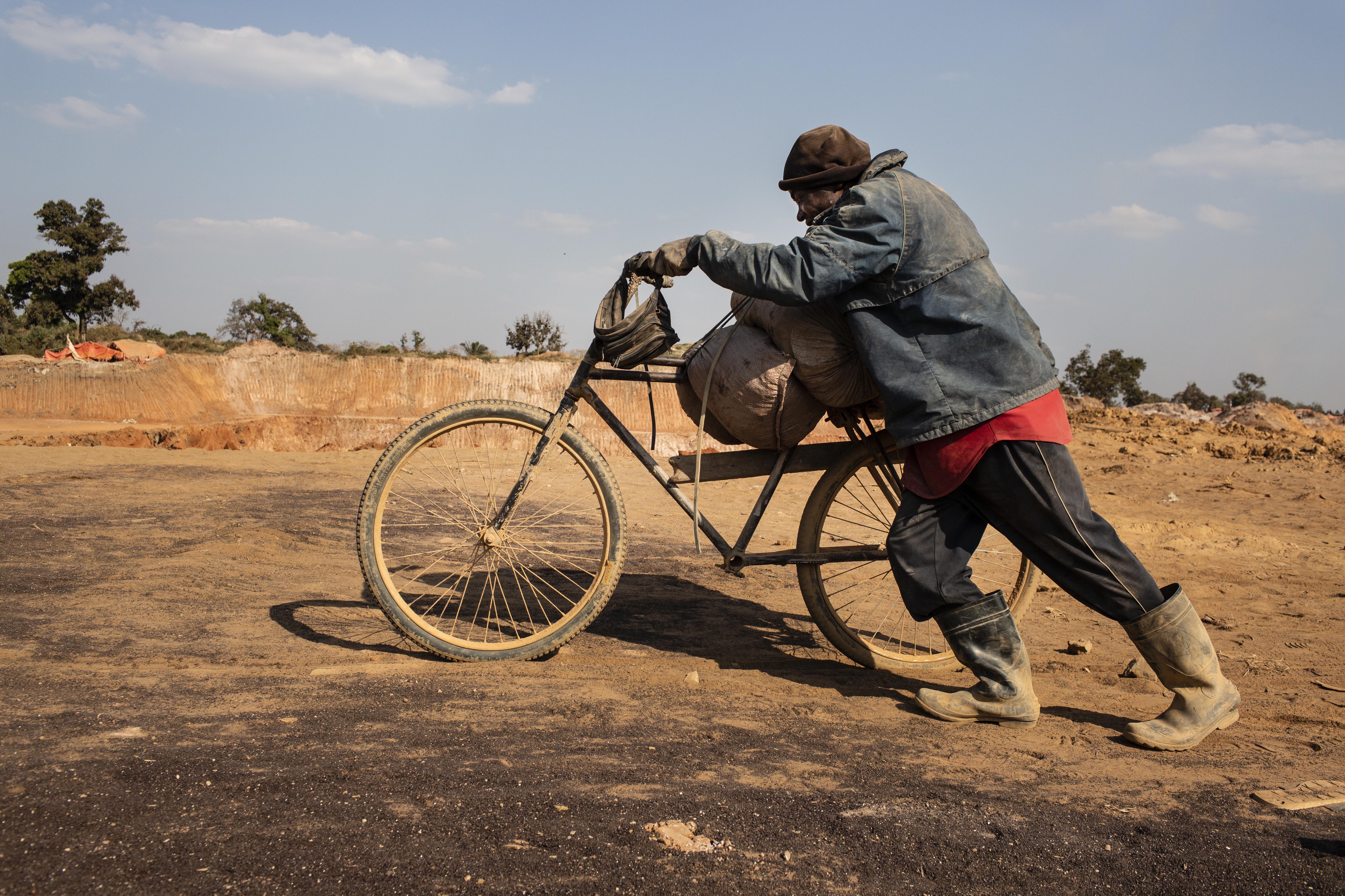 A miner pushes a bicycle piled with sacks of cobalt from a mining pit to the depot inside the CDM (Congo DongFang International Mining) Kasulo mine. Image by Sebastian Meyer. Congo, 2018. Media file: sebastian_meyer_cobalt_11.jpg