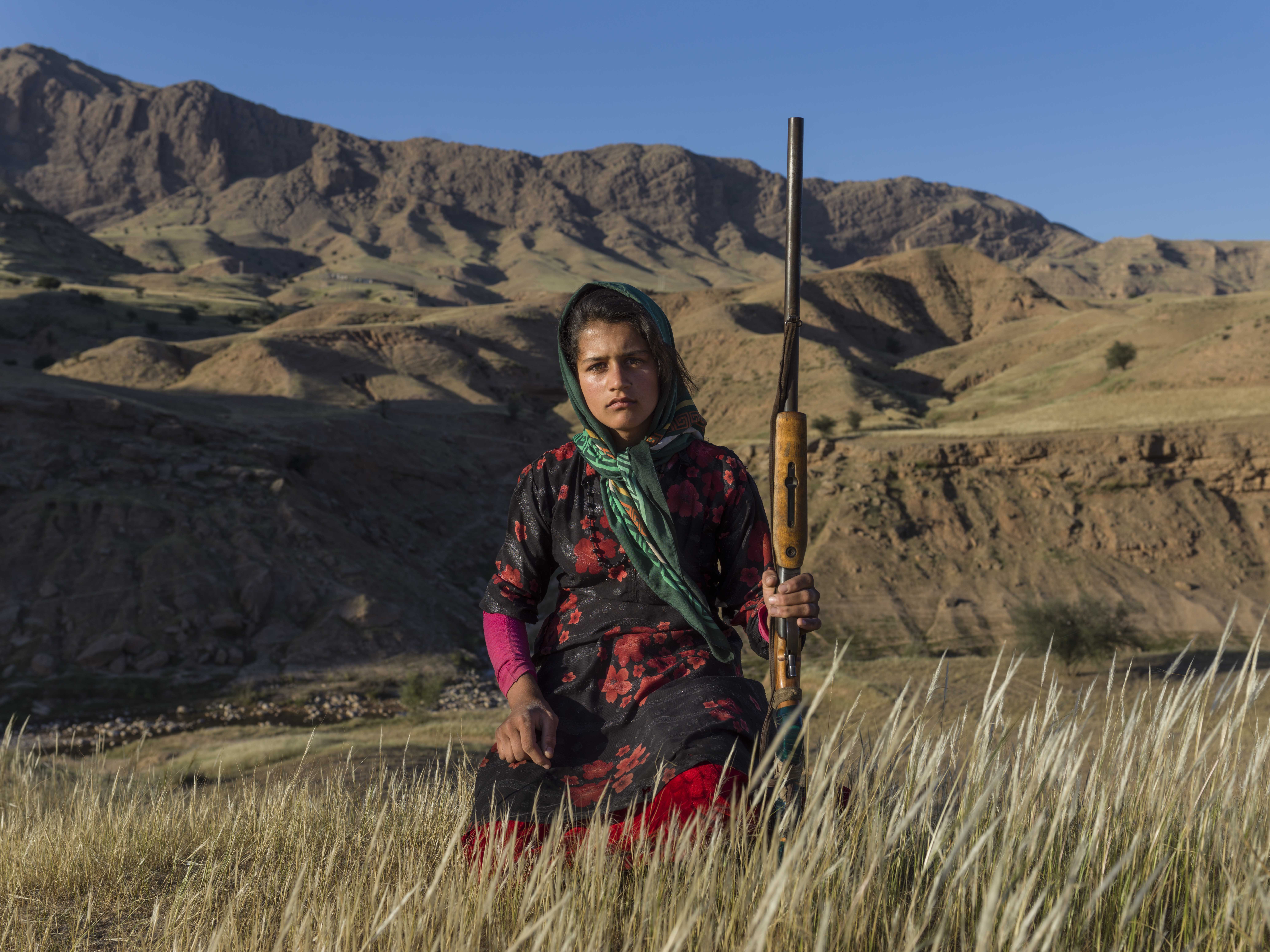 Masoumeh Ahmadi, 14 years old, wants to be called by the name Golbahar since Masoumeh is an old-fashioned name, not popular among the young generation. She stands in Chamsoor lands in Khuzestan Province holding a gun. It is common among Bakhtiaris for each person to own a gun. Each family might have three or 4fourguns that are mostly for men. Women—with the approval of their husband and father—can have their own guns after they marry . Many of them receive their gun as a gift from their husbands after they give birth to their first son. Masoumeh borrowed her mother’s gun occasionally. Image by Newsha Tavakolian. Iran, 2018. Masoumeh Ahmadi, 14 years old, wants to be called by the name Golbahar since Masoumeh is an old-fashioned name, not popular among the young generation. She stands in Chamsoor lands in Khuzestan Province holding a gun. It is common among Bakhtiaris for each person to own a gun. Each family might have three or 4fourguns that are mostly for men. Women—with the approval of their husband and father—can have their own guns after they marry . Many of them receive their gun as a gift from their husbands after they…