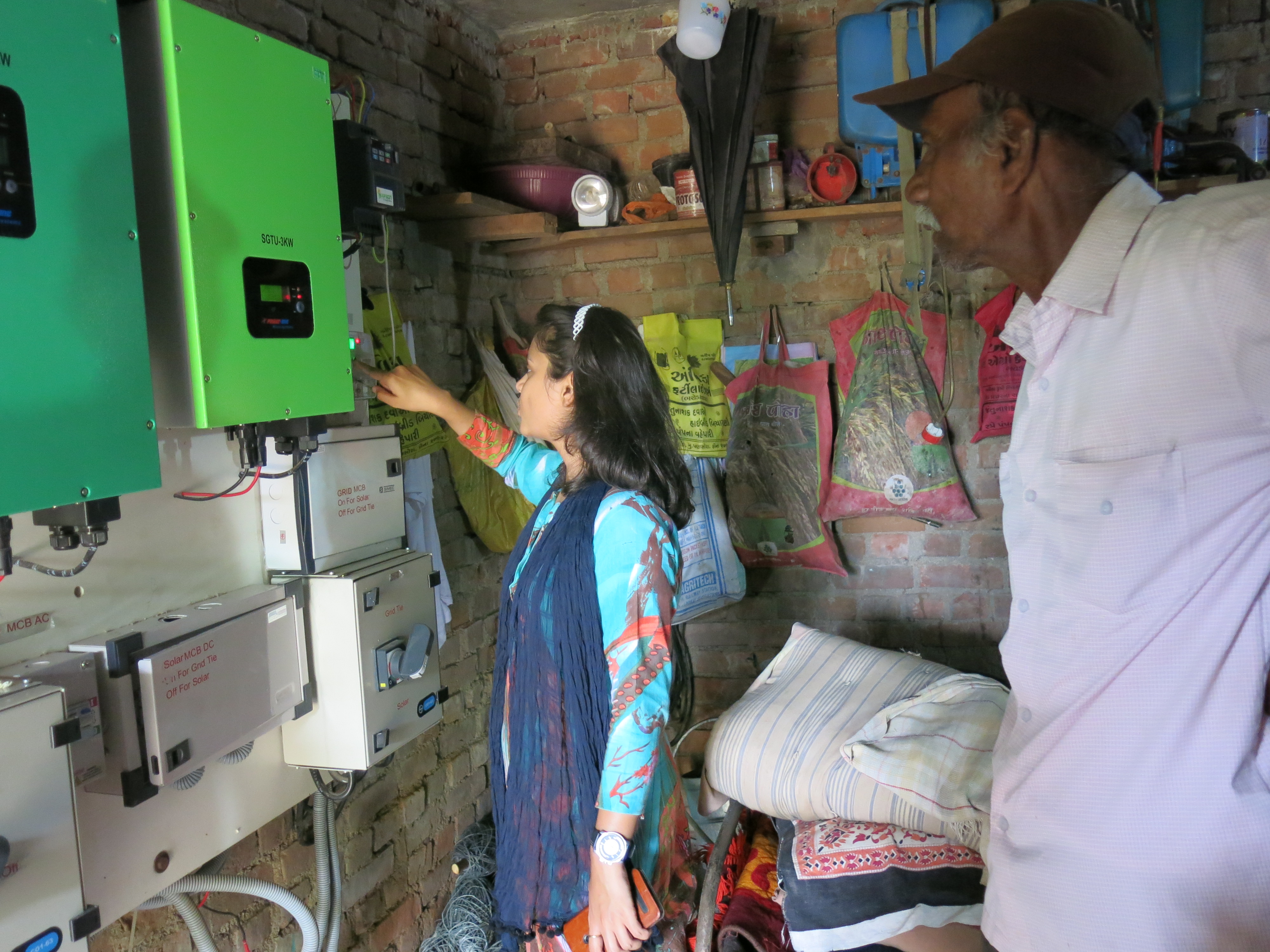 Neha Durga, a program associate with the International Water Management Institute, examines the net metering of farmer Raman Bhai Parmar's solar panels. Image by Lisa Palmer. India, 2015. Media file: img_1699.jpg
