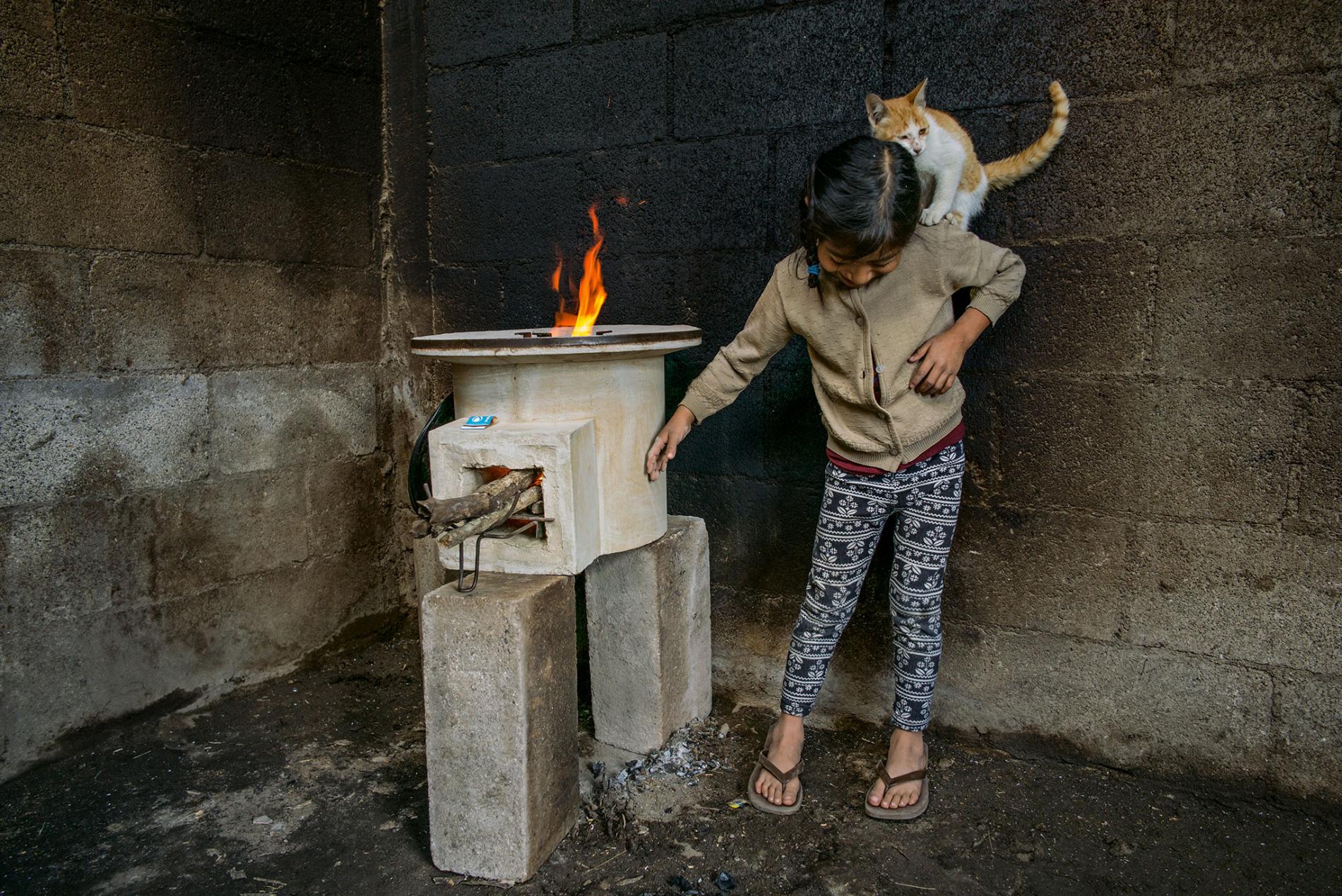 Tania López, 7, plays with her cat in a room whose walls were blackened by an old open fire; the new stove, provided by StoveTeam International, is efficient and safe to touch. Image by Lynn Johnson. Guatemala, 2017. Tania López, 7, plays with her cat in a room whose walls were blackened by an old open fire; the new stove, provided by StoveTeam International, is efficient and safe to touch. Image by Lynn Johnson. Guatemala, 2017.