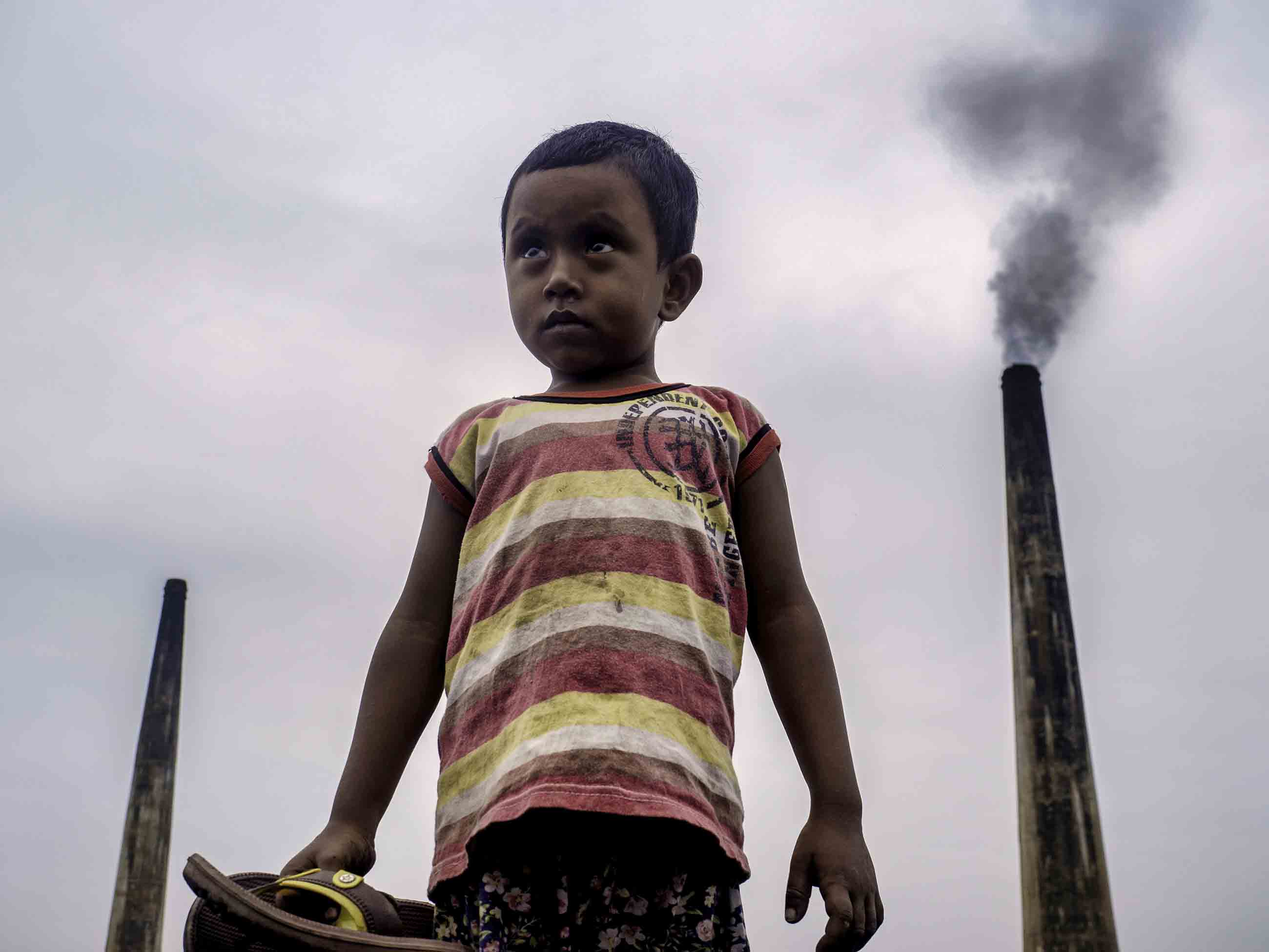 Four-year-old Nayem often plays atop large piles of coal used to fire kilns at a brick factory at the edge of Dhaka, Bangladesh. The chimneys from such factories contribute to some of the worst air pollution in the world. Image by Larry C. Price. Bangladesh, 2018. Four-year-old Nayem often plays atop large piles of coal used to fire kilns at a brick factory at the edge of Dhaka, Bangladesh. The chimneys from such factories contribute to some of the worst air pollution in the world. Image by Larry C. Price. Bangladesh, 2018.