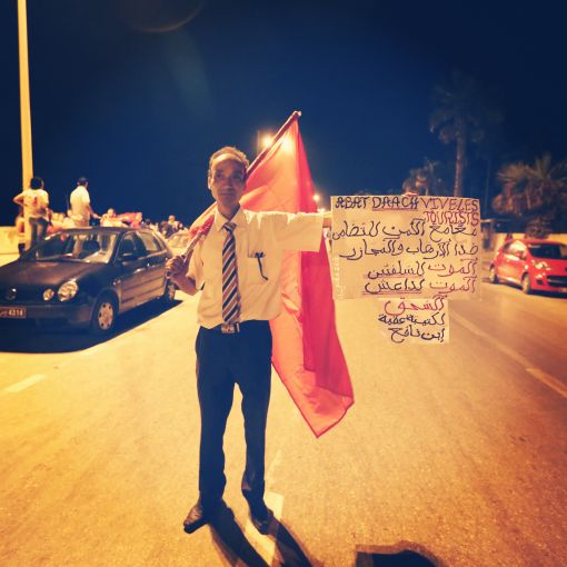 At a protest the evening following a mass beach shooting attack, a Tunisian man in Sousse holds up a banner in French and Arabic condemning ISIL and showing solidarity with the foreign tourists who were targeted. Image by Alice Su. Tunisia, 2015. At a protest the evening following a mass beach shooting attack, a Tunisian man in Sousse holds up a banner in French and Arabic condemning ISIL and showing solidarity with the foreign tourists who were targeted. Image by Alice Su. Tunisia, 2015.