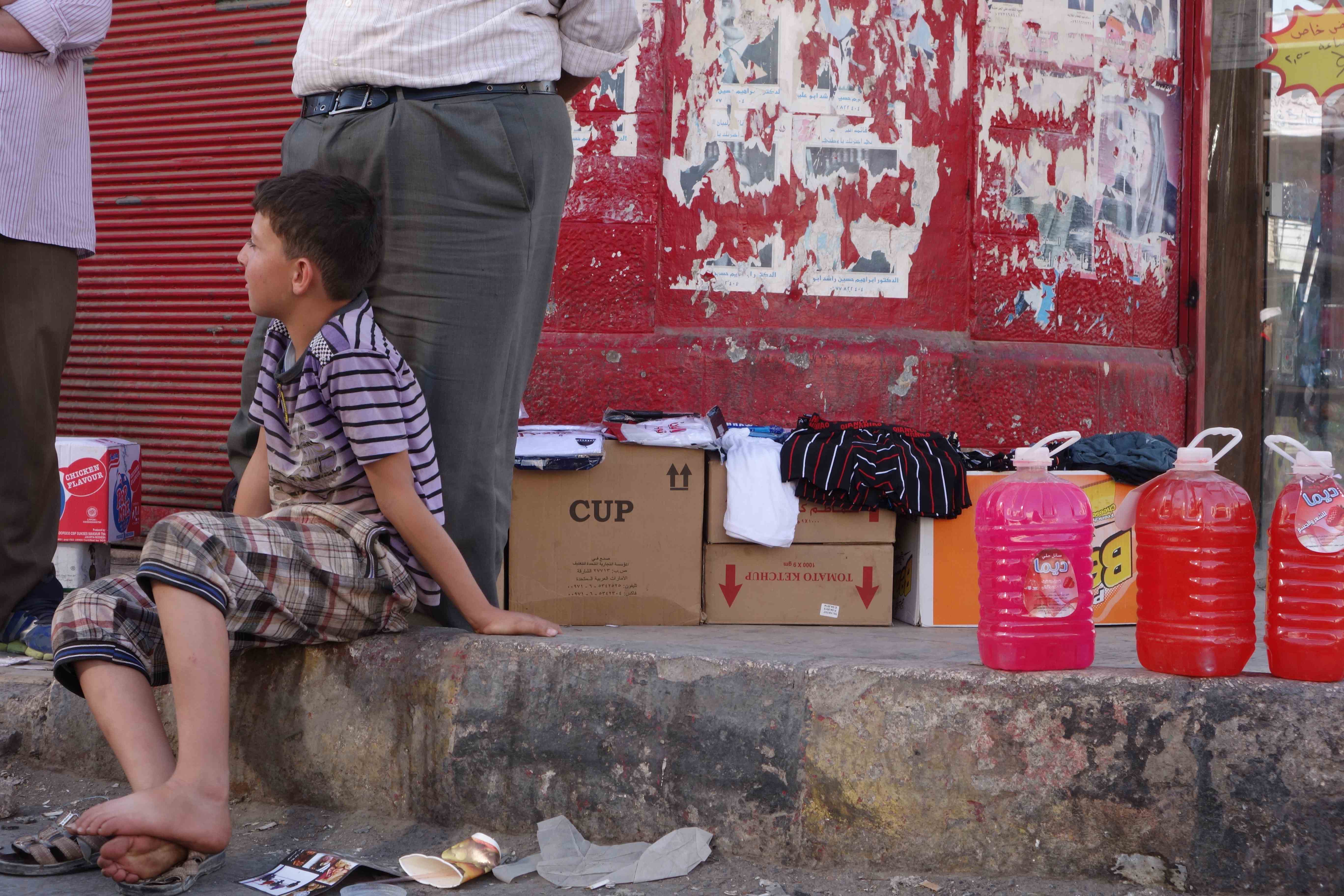 Like many Syrian refugee children, this boy in Mafraq, Jordan, has to work instead of going to school. Selling household products in the street is a common job for them. Image by Alisa Roth. Syria, 2013.