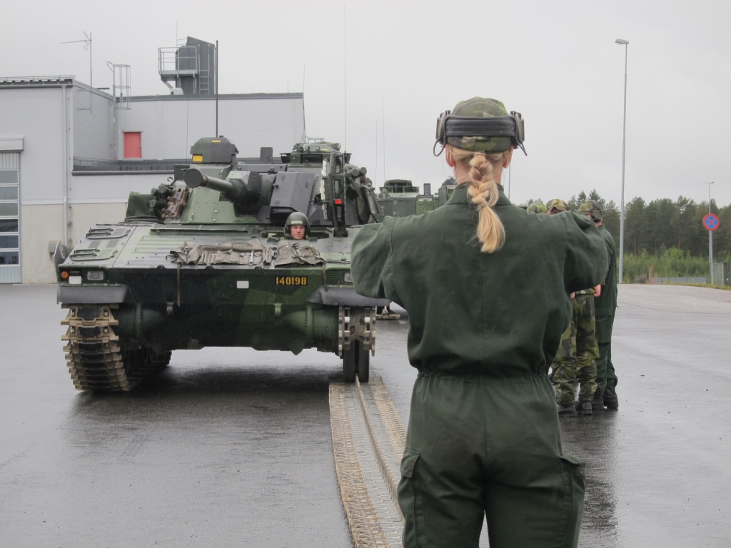 A female mechanized infantry conscript directs colleagues while learning to repair a CV90 combat vehicle. Image by Teresa Fazio. Sweden, 2018. A female mechanized infantry conscript directs colleagues while learning to repair a CV90 combat vehicle. Image by Teresa Fazio. Sweden, 2018.