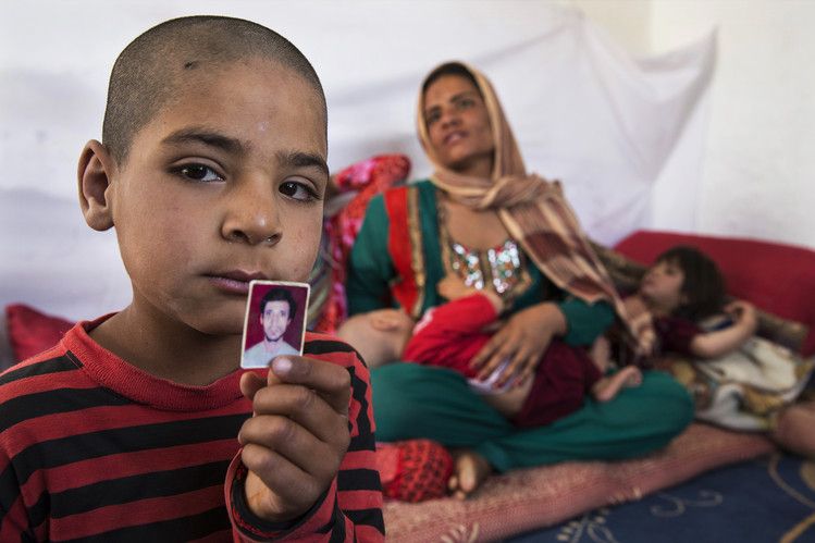 Hamid, in 2014, holds a photo of his father, who was killed during his service in the Afghan army, leaving Fereshta, at rear, widowed with five children. Image by Paula Bronstein/The Wall Street Journal. Afghanistan, 2014.
