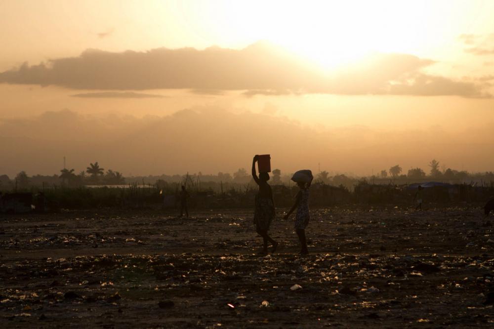 From Meghan Dhaliwal's student fellow project: Two women cross a field in Cité Soleil. They carry necessities for the day on their heads. Image by Meghan Dhaliwal. Haiti, 2012. Media file: dhaliwal-10_dark.jpg