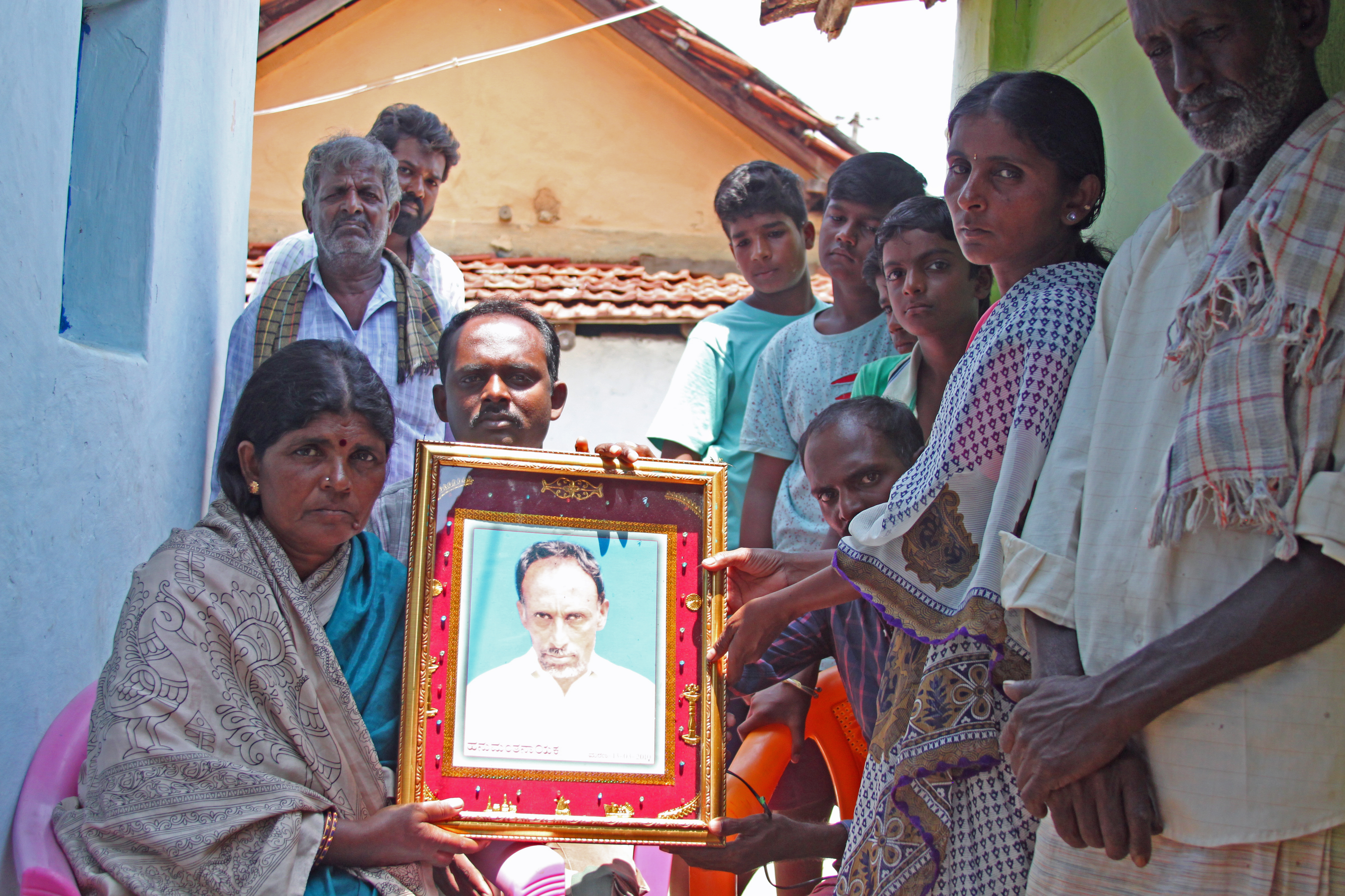 Gopamma Nayaka, surrounded by family and neighbors, holds the portrait of her husband Hanamuantha, who was killed and eaten by a tiger in India's Bandipur National Park and Tiger Reserve. Image by Rachel Nuwer. India, 2019. Gopamma Nayaka, surrounded by family and neighbors, holds the portrait of her husband Hanamuantha, who was killed and eaten by a tiger in India's Bandipur National Park and Tiger Reserve. Image by Rachel Nuwer. India, 2019.