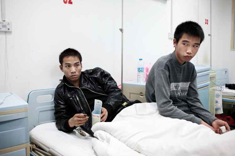 Ling Shi Ling, 23, and Liu Wei, 18, recovering at a government hospital from on-the-job hand injuries. Liu's injury was from the factory's removal of a machine protection shield (which increased productivity 50-60 percent). His uncle owns 30 percent of the factory and is the only one of the four factory owners willing to cover his medical expenses. Image by Jocelyn Baun, China, 2011. image