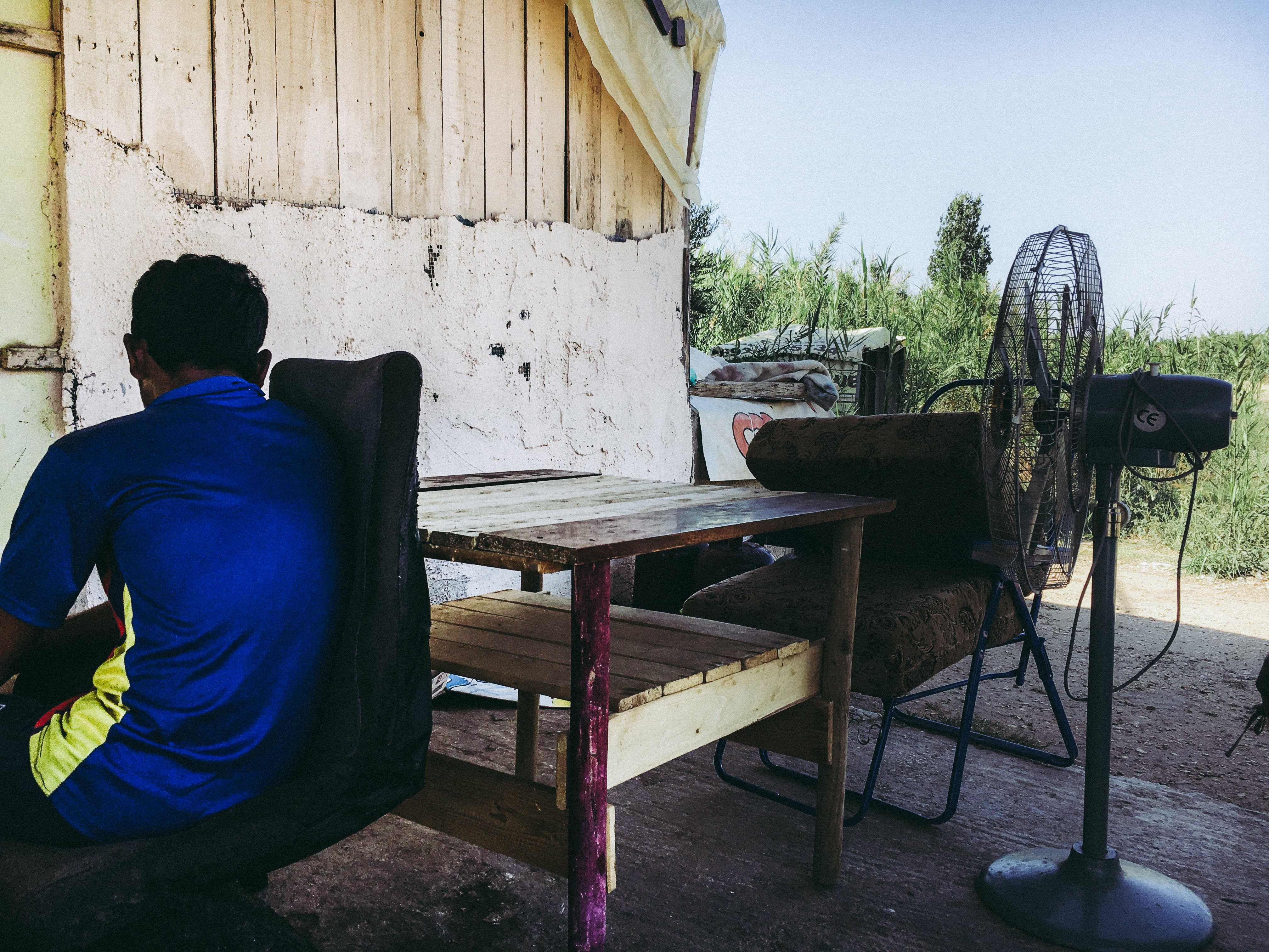 An unaccompanied minor sits in front of a migrants' shack in Marathona Village. Image by Divya Mishra. Greece, 2018. An unaccompanied minor sits in front of a migrants' shack in Marathona Village. Image by Divya Mishra. Greece, 2018.