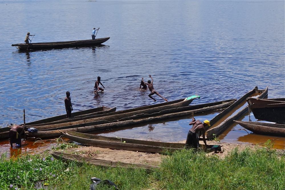 Boys swimming off pirogues along the Mbandaka waterfront. This is a city of around 800,000 people, a major regional capital, but there are few cars, no central electricity, and little running water. At night the streets are nearly pitch black, the only light the faint glow of charcoal fires. Image by Jon Sawyer. Democratic Republic of Congo, 2013.