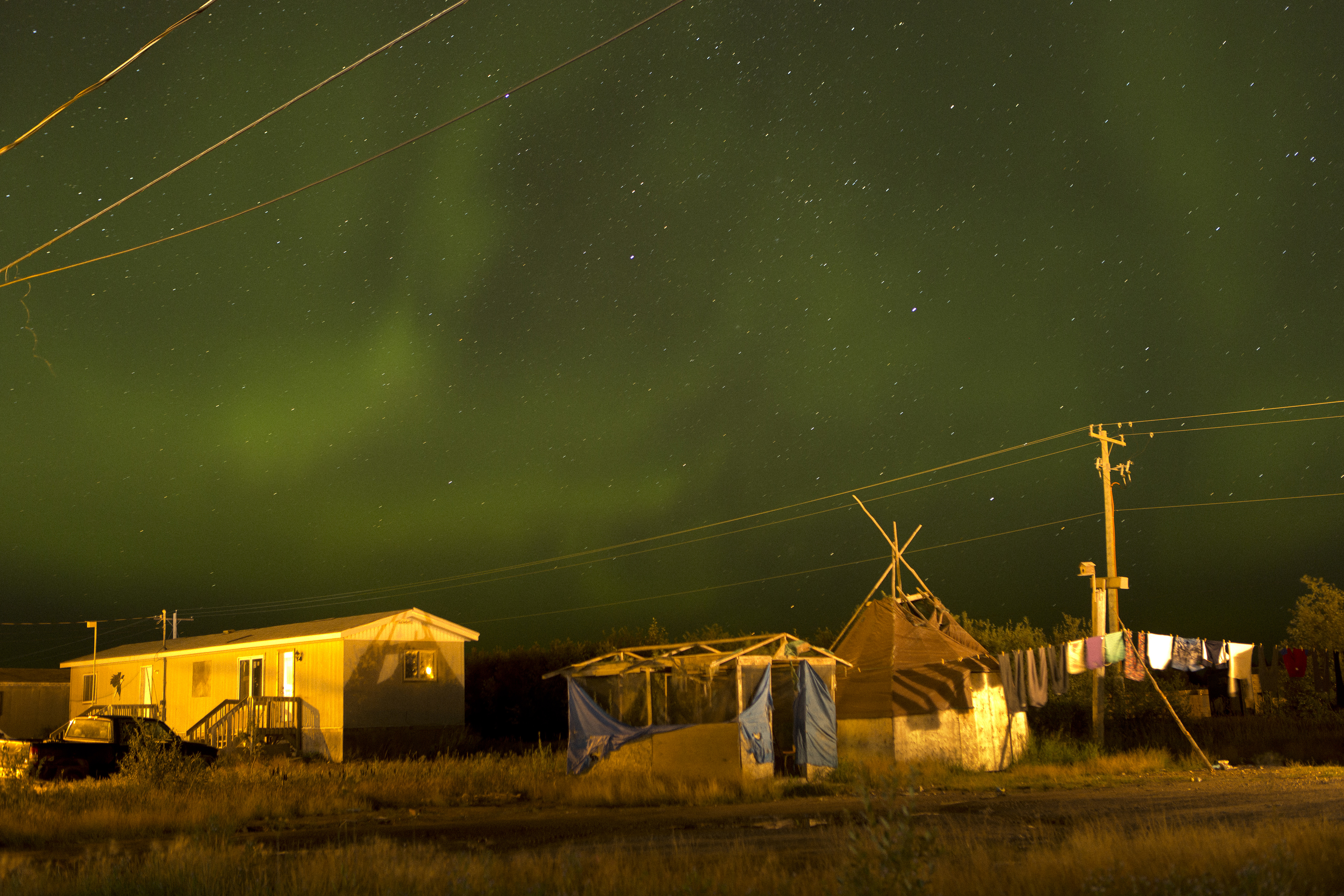 The northern lights fill the sky over the remote First Nations community of Attawapiskat. Attawapiskat is an isolated First Nation community located in northern Ontario, Canada, at the mouth of the Attawapiskat River on James Bay. On April 9, 2016, the community of approximately 2,000 people declared a state of emergency after being overwhelmed with attempted suicides, over 100 attempts in a 10-month period. Image by David Maurice Smith/Oculi. Canada, 2016. David Maurice Smith_Attawapiskat_Pulitzer Grant