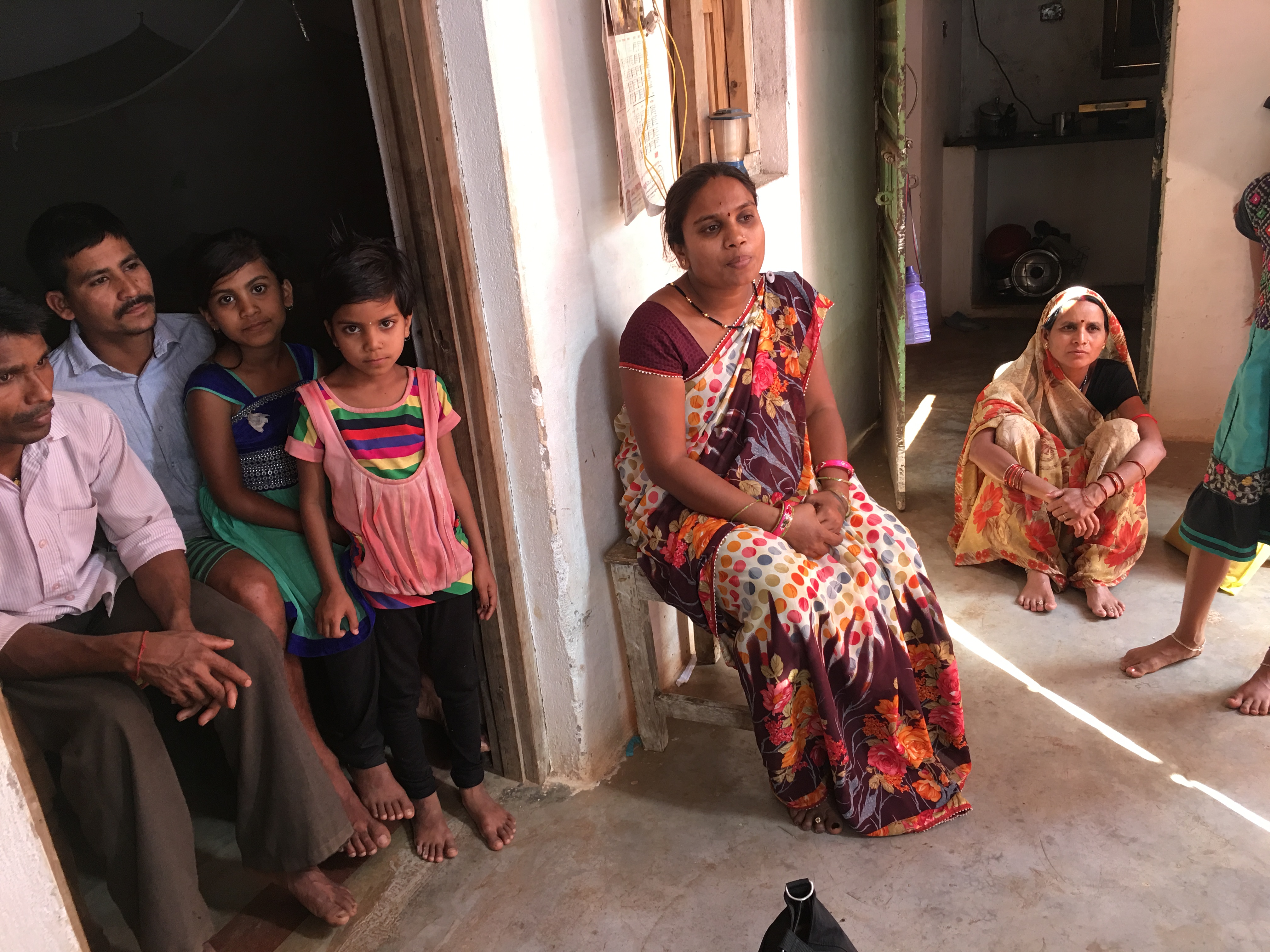 Pinki Sahu sits in a chair surrounded by family members. Pinki lost her sister, Sunita, when she died due to a botched sterilization procedure at a government-run camp in Chhattisgarh. Image by Hannah Harris Green. India, 2018. Pinki Sahu sits in a chair surrounded by family members. Pinki lost her sister, Sunita, when she died due to a botched sterilization procedure at a government-run camp in Chhattisgarh. Image by Hannah Harris Green. India, 2018.
