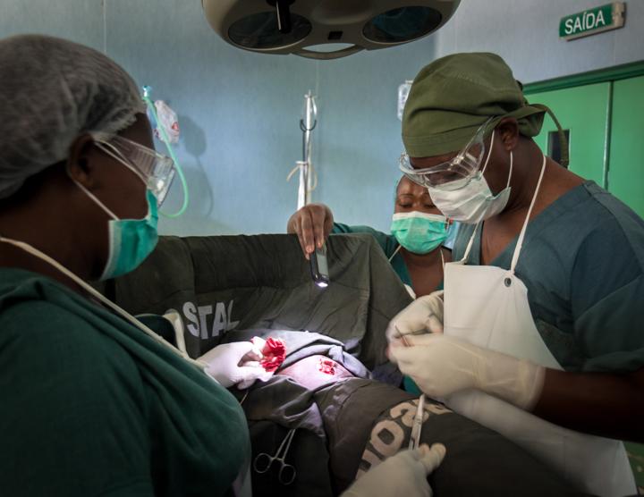Victor Muitiquile closes a stab would by the light of a cellphone after the power went out at Chokwe District Hospital in Mozambique. Image by Bridget Huber. Mozambique, 2014. Media file: moz_lil-0248.jpg