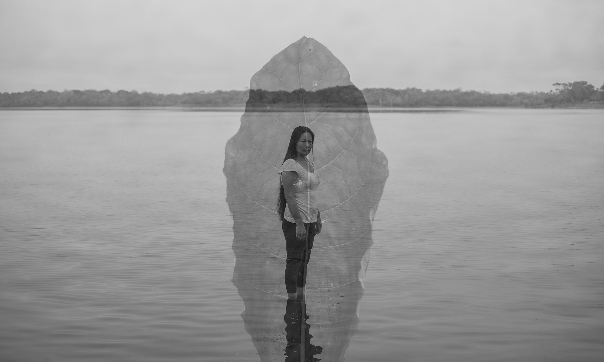 Imagem de Florence Goupil. Black and white double exposure photo of a woman standing in front of a body of water with a leaf superimposed on the image.