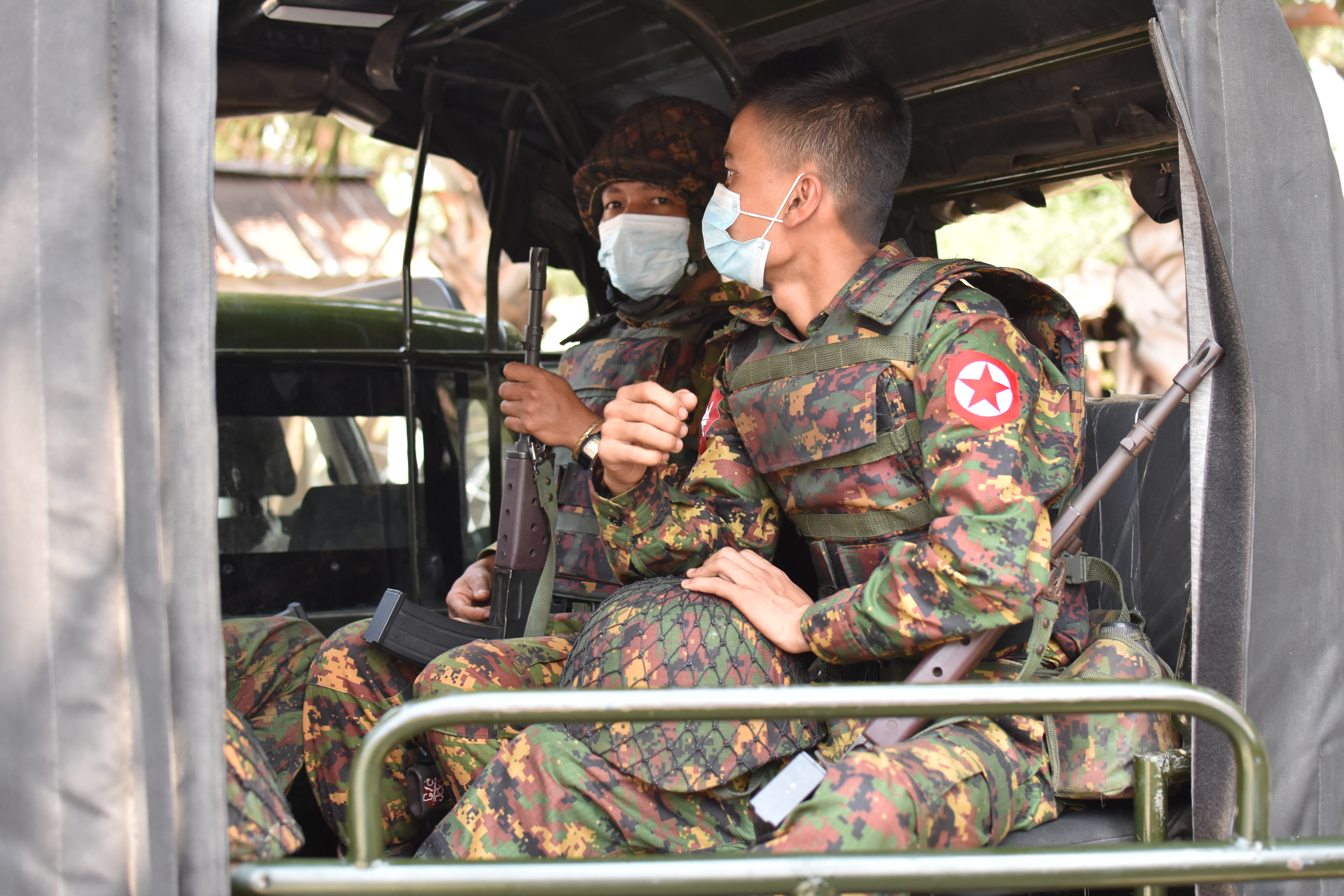 Soldiers wearing medical masks sit in a vehicle.