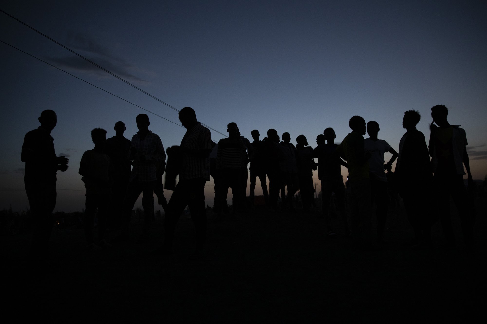 tigray.jpeg About 20 men stand outside at nighttime. We can only see their silhouettes against the night sky.