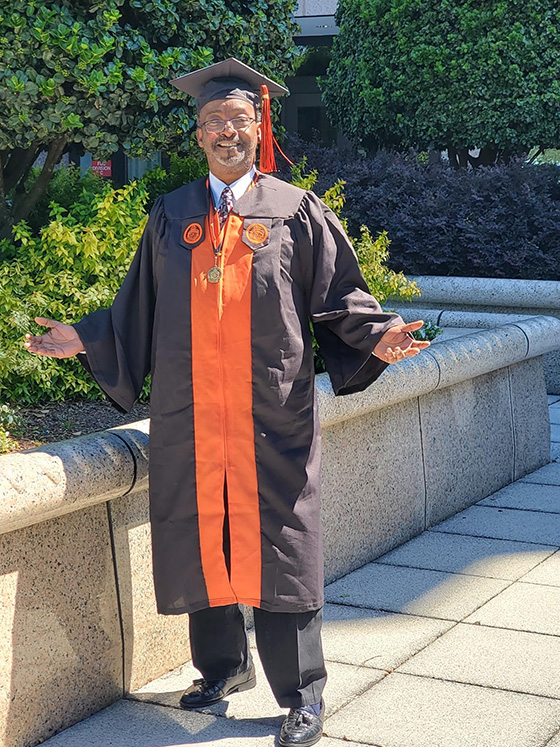 Michael Watkins stands outside in a graduation cap and gown.