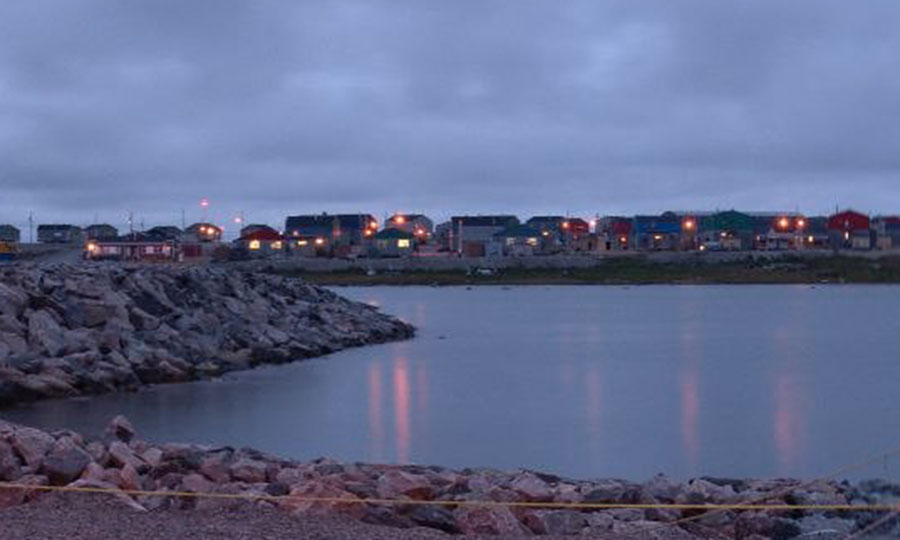 Web-2.jpeg Buildings glow with lights in the distance, behind a body of water.