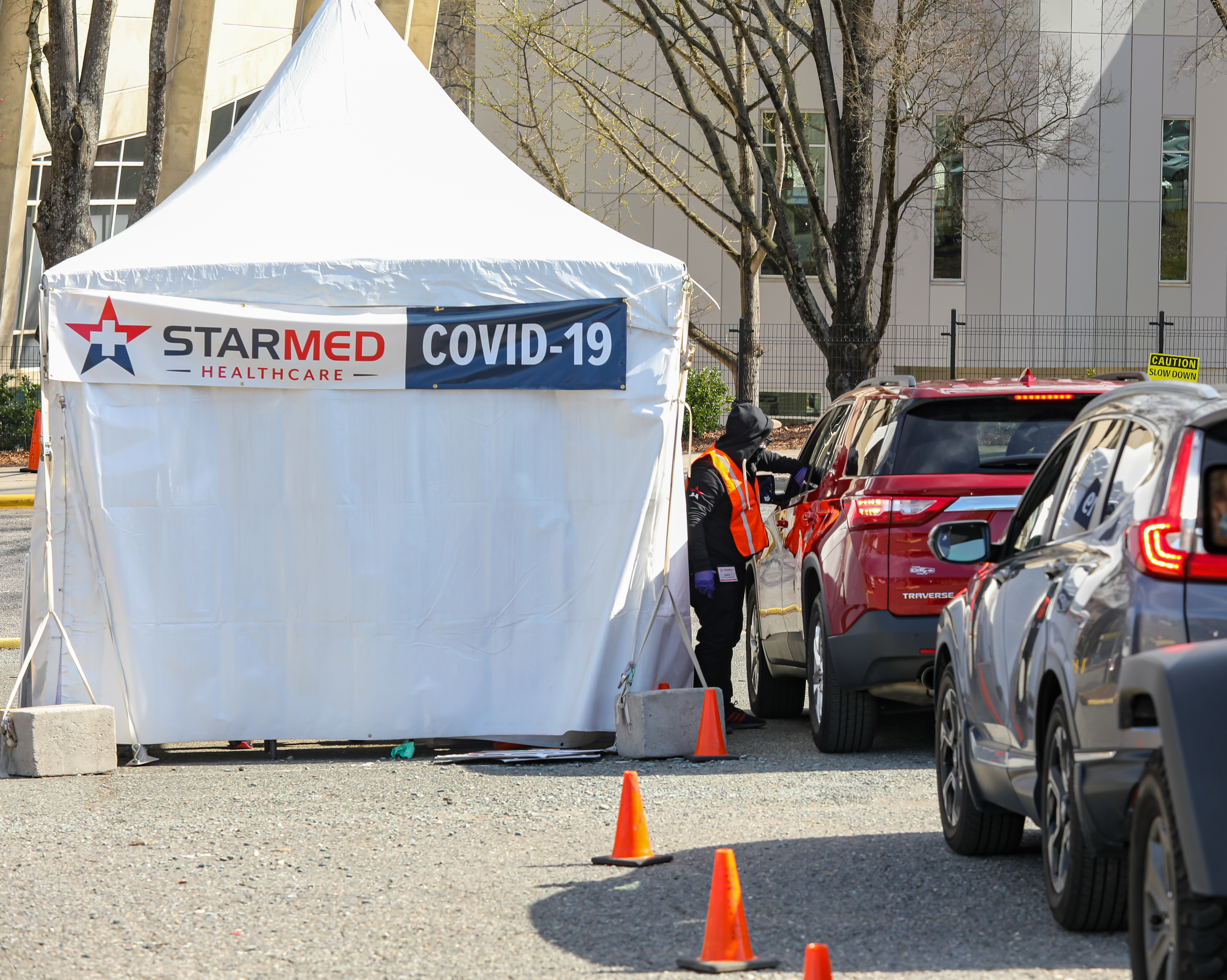 shutterstock_1940275600.jpeg Vehicles line up next to a white tent that has a banner reading, "Starmed Healthcare COVID-19."
