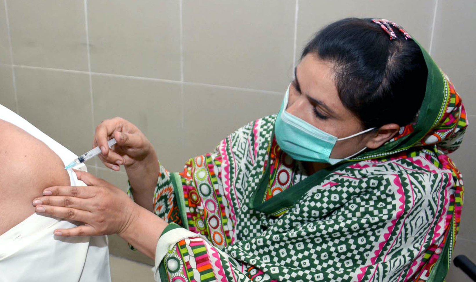shutterstock_1963716649 copy.jpg A health worker in PPE gives someone a vaccine.