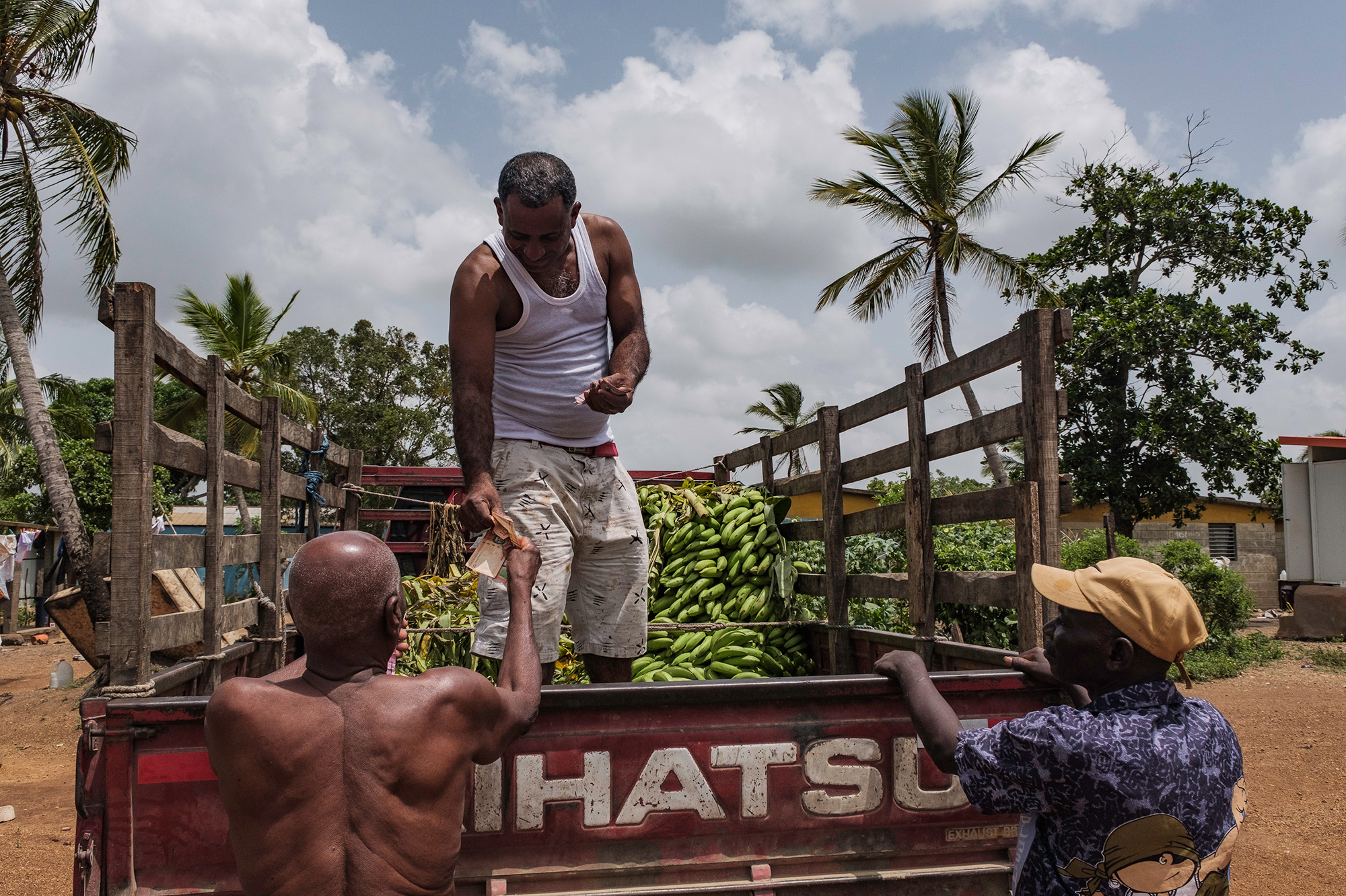 A man stands on a truck with plantains talking to two other men standing on the ground