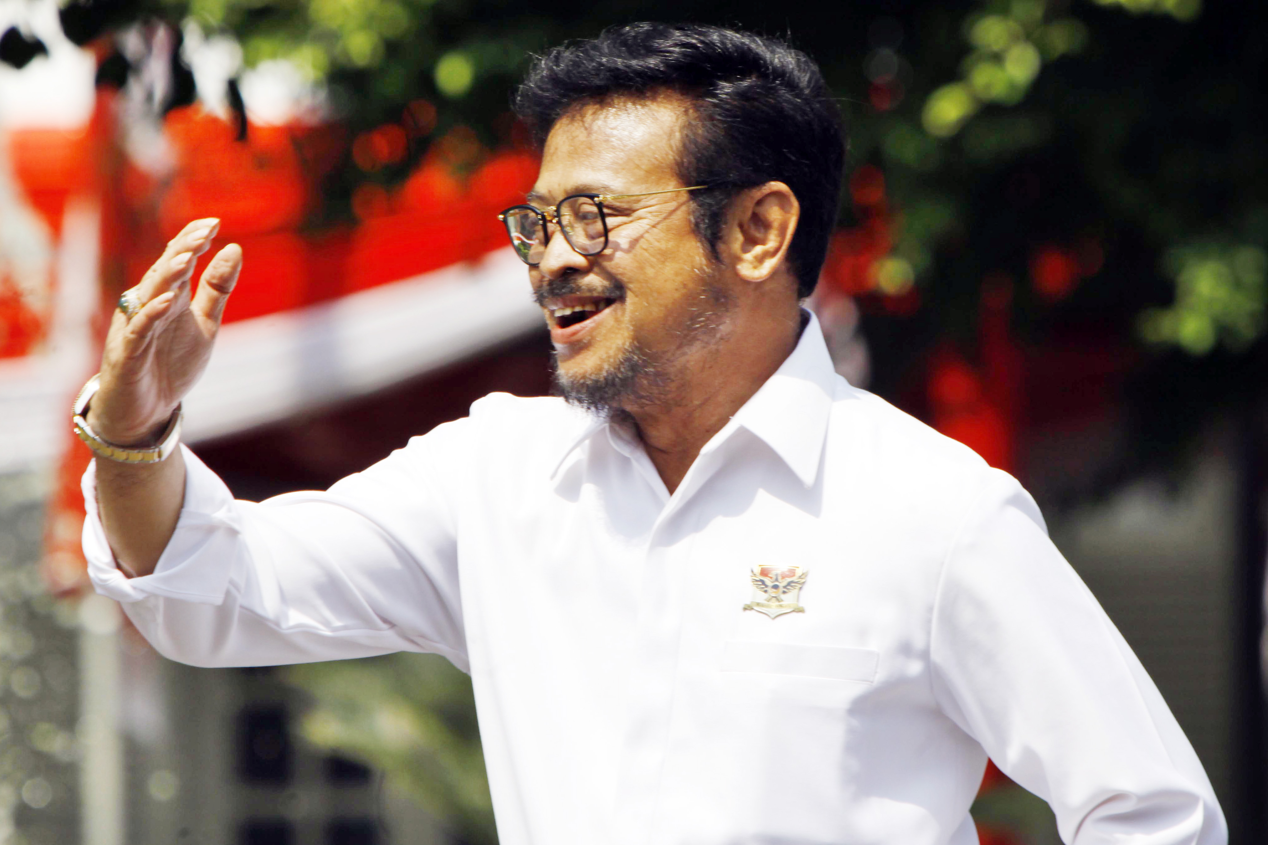 Agriculture Minister Syahrul Yasin Limpo waves while walking in front of the flag of Indonesia
