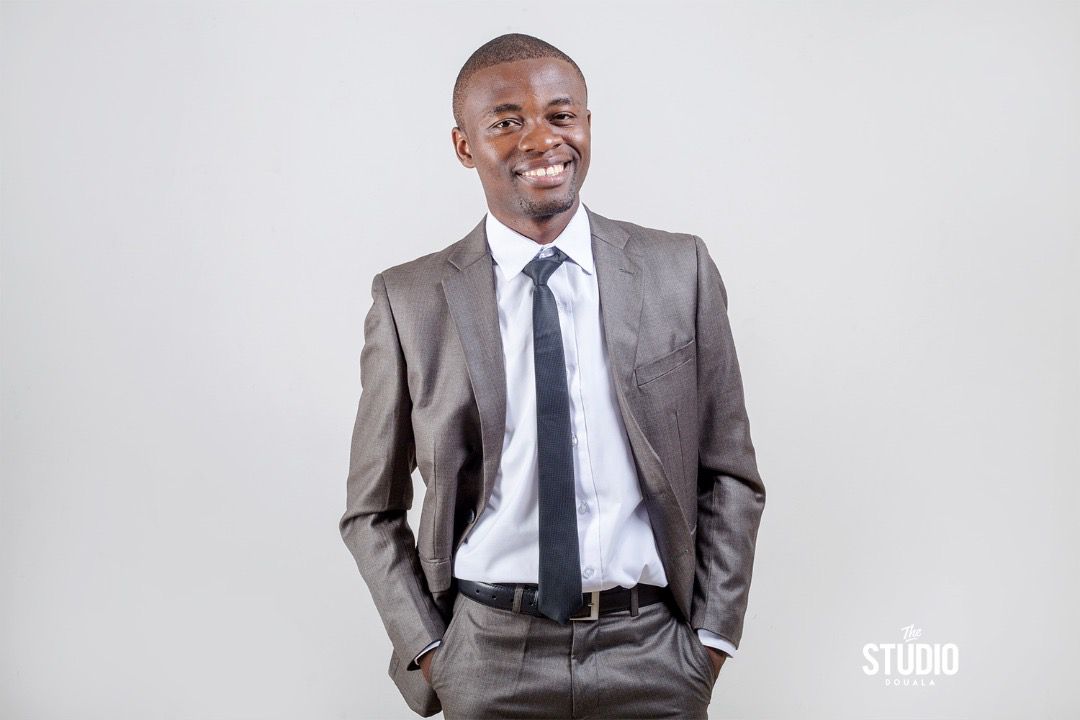 A person wearing a grey jacket, white shirt, and black tie smiles at the camera.