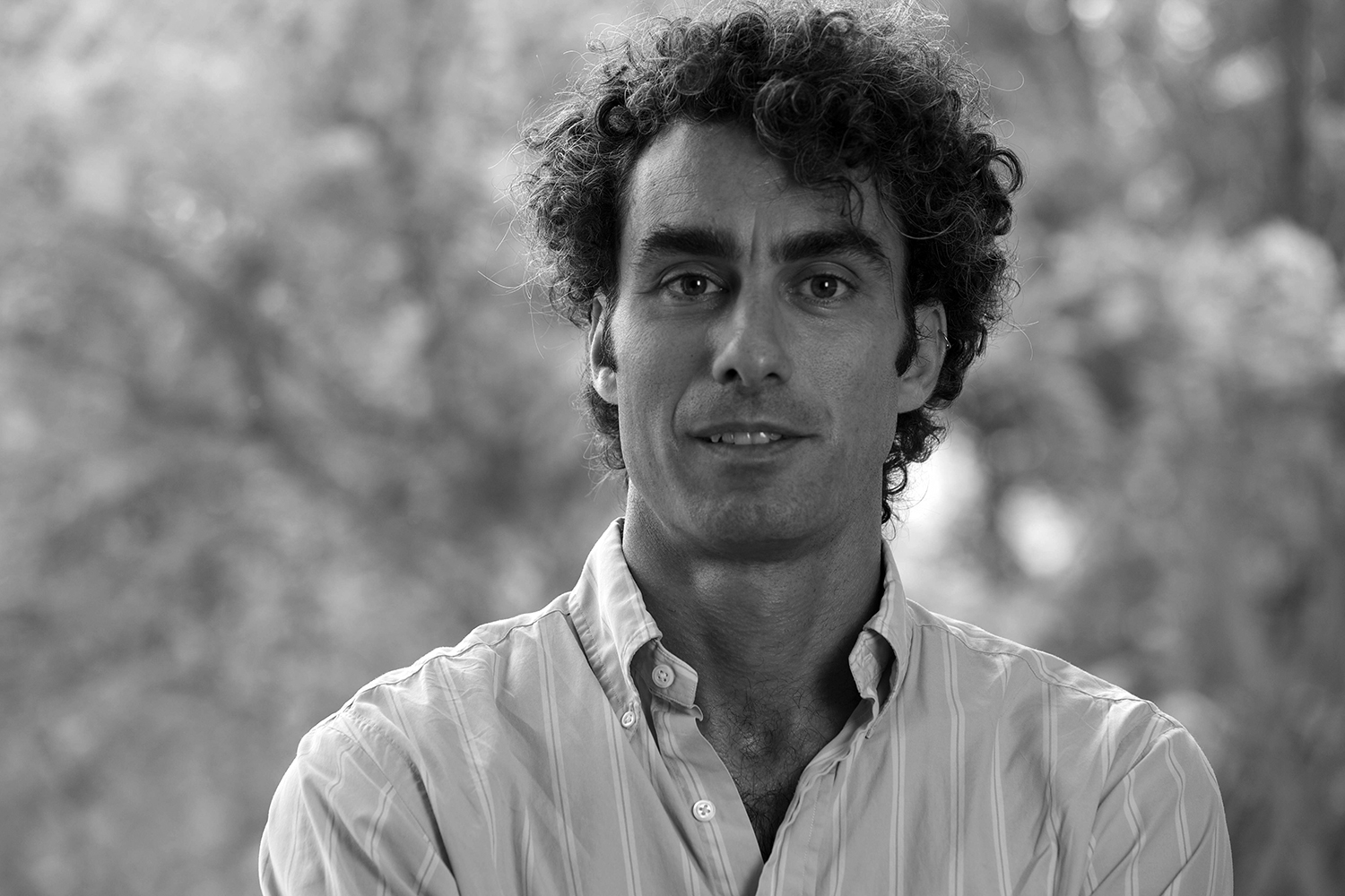 A man with curly hair and wears a white shirt smiles at the camera.