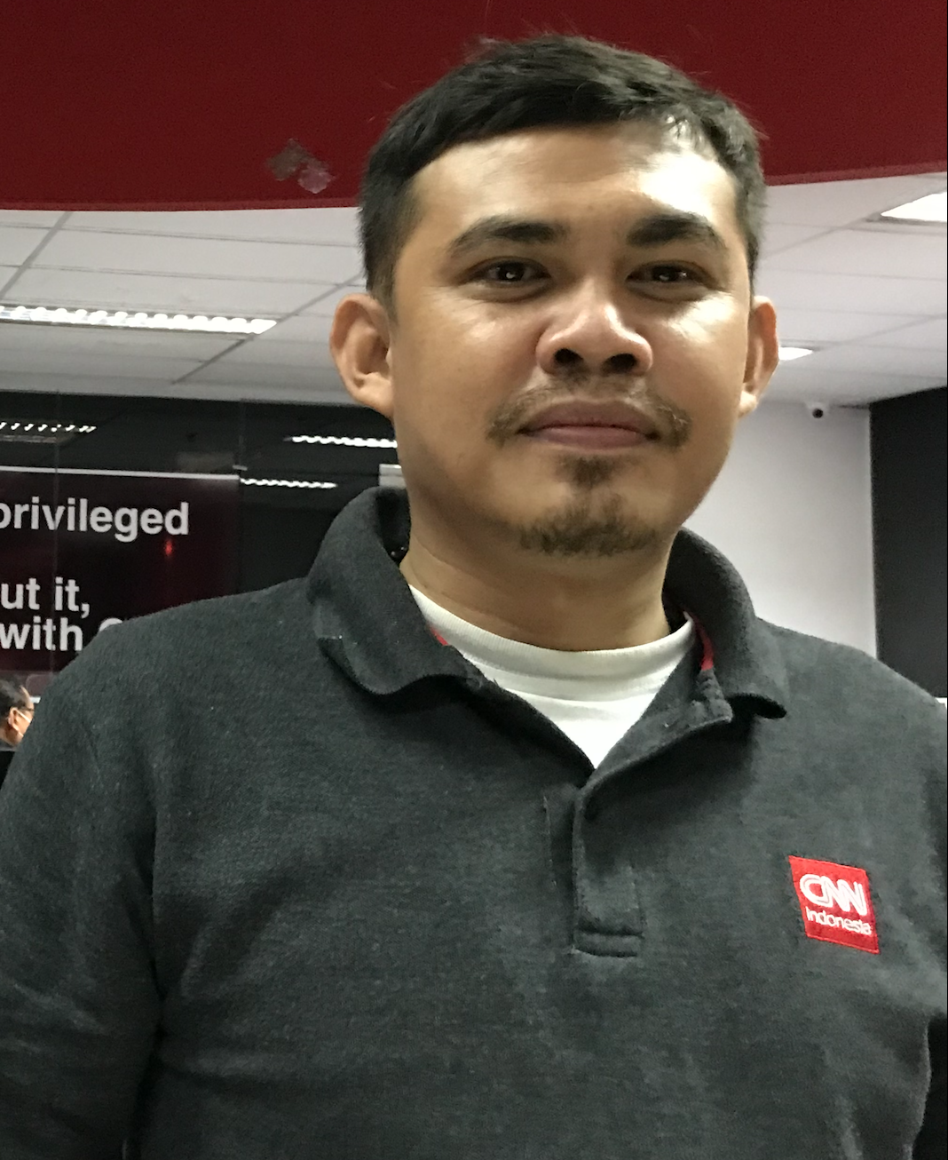 A person wears a black shirt with a red patch logo.