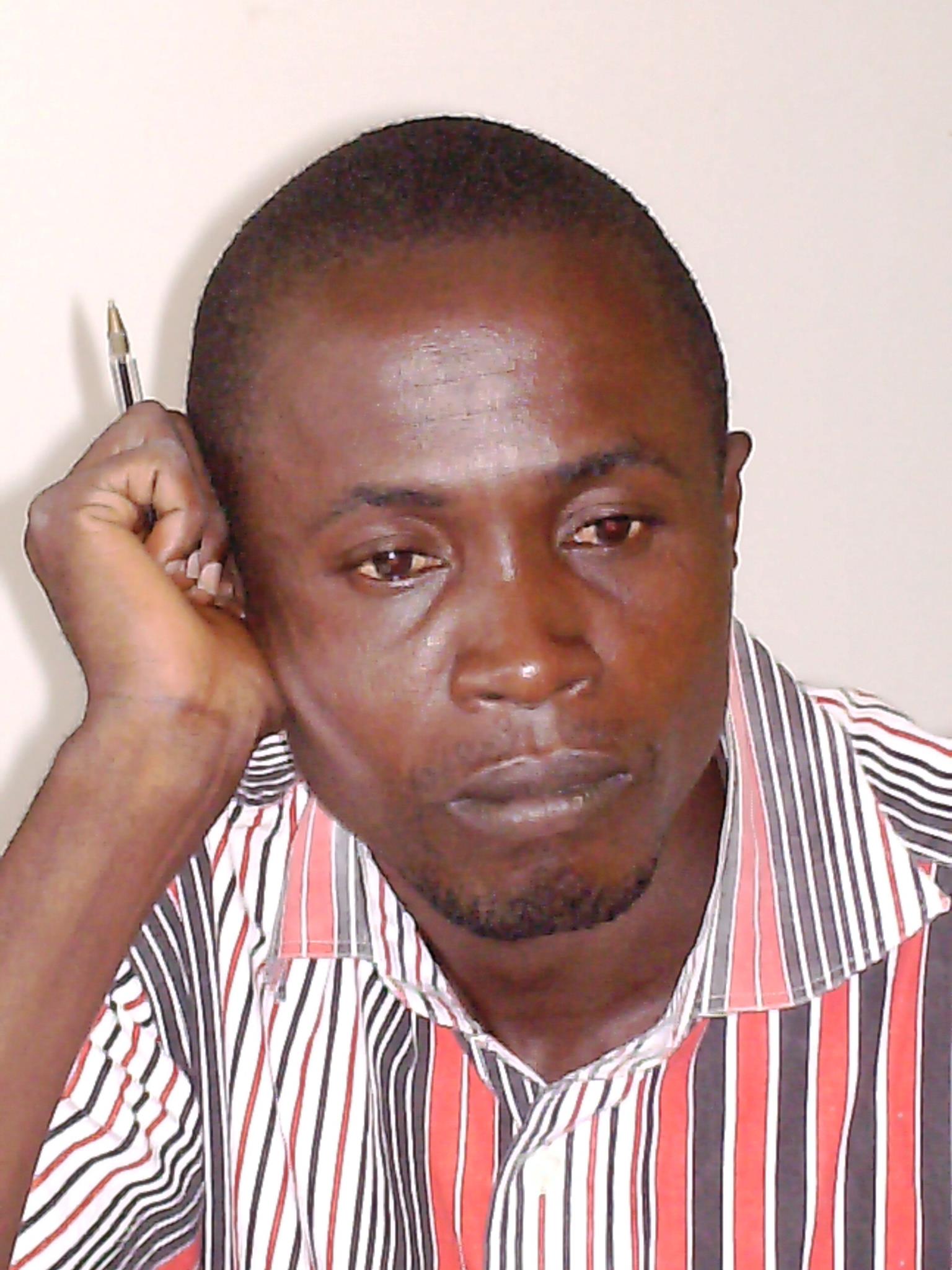 A person wears a red and white patterned shirt. The person is also holding a pen.