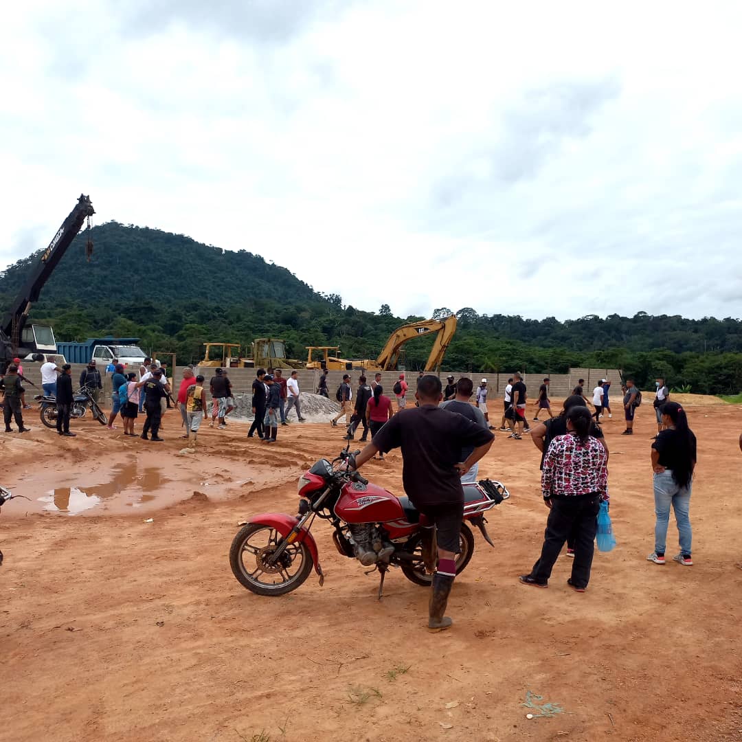 A crowd of people stand and look at the deforested mining area.