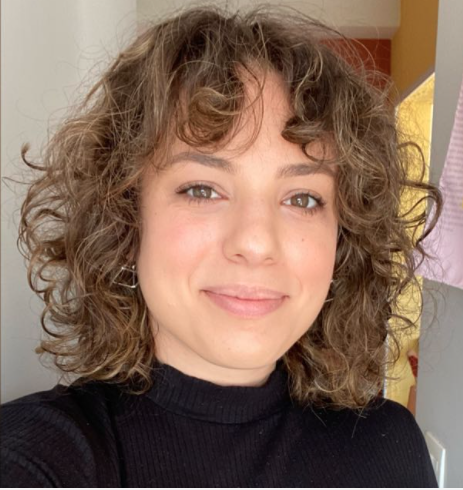 A woman with curly hair and brown eyes stares into the lens