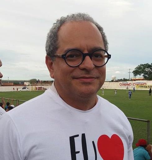 A man with grey curly hair and glasses stares into the camera