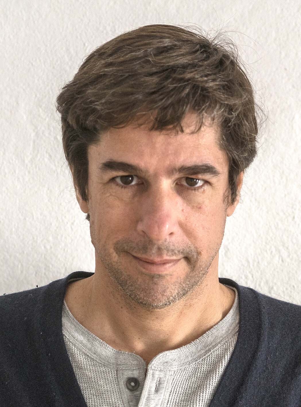 A man with short brown hair, a black sweater and grey shirt.