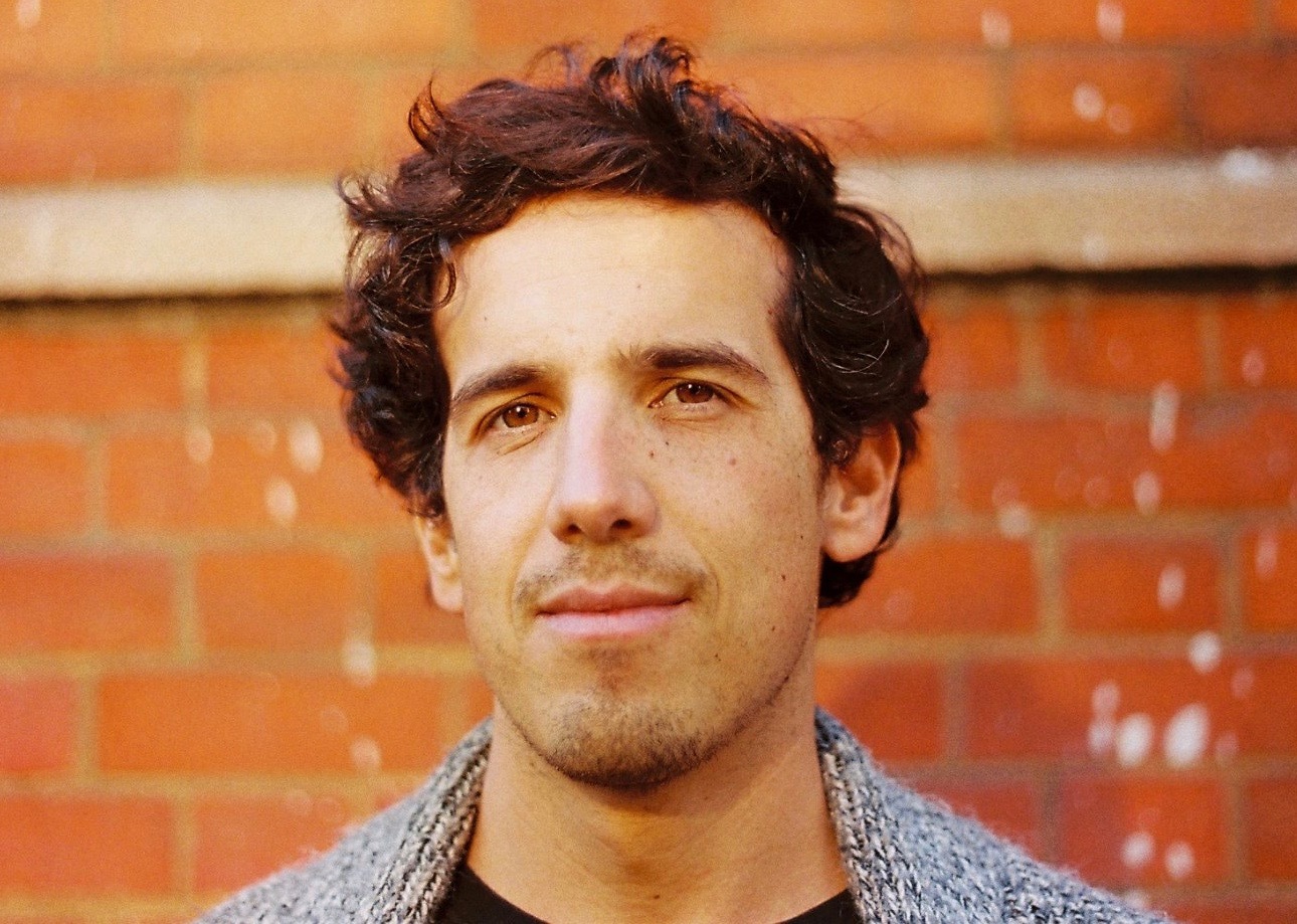 A person has curly brown hair and wears a grey jacket.