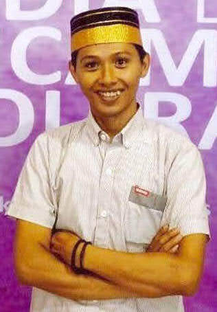 A man wears a grey shirt and an Indonesian, black songkok hat.