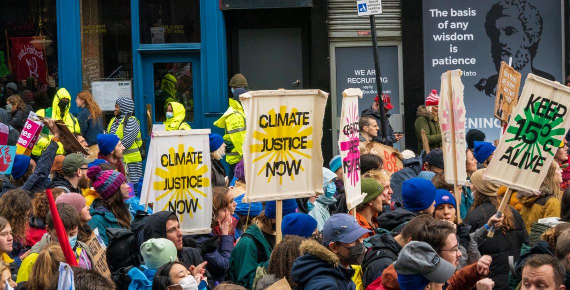 795518a7-80dc-7769-d8a7-0e35610062c7.jpeg Protestors hold signs reading "Climate justice now".