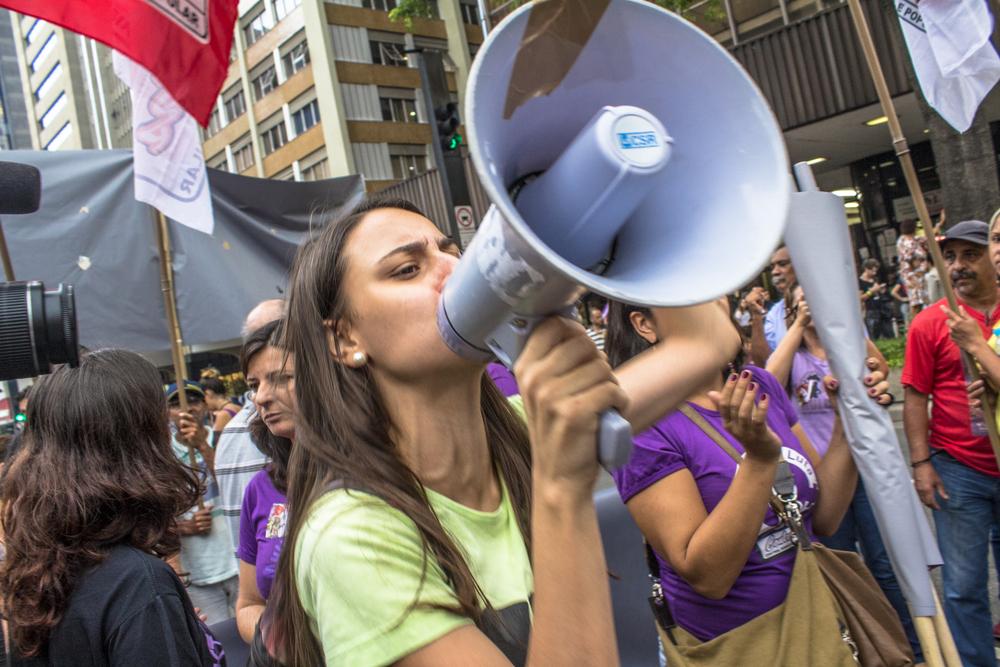 a woman surrounded by protesters and flags shouts through a megaphone