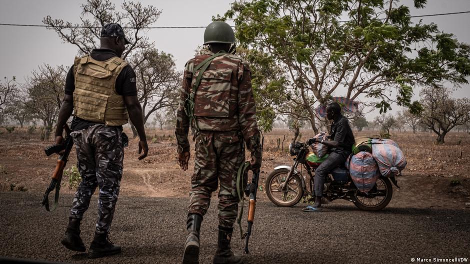 Beninese Military Checkpoint Two soldiers carrying automatic rifles stop a man on a motorbike.