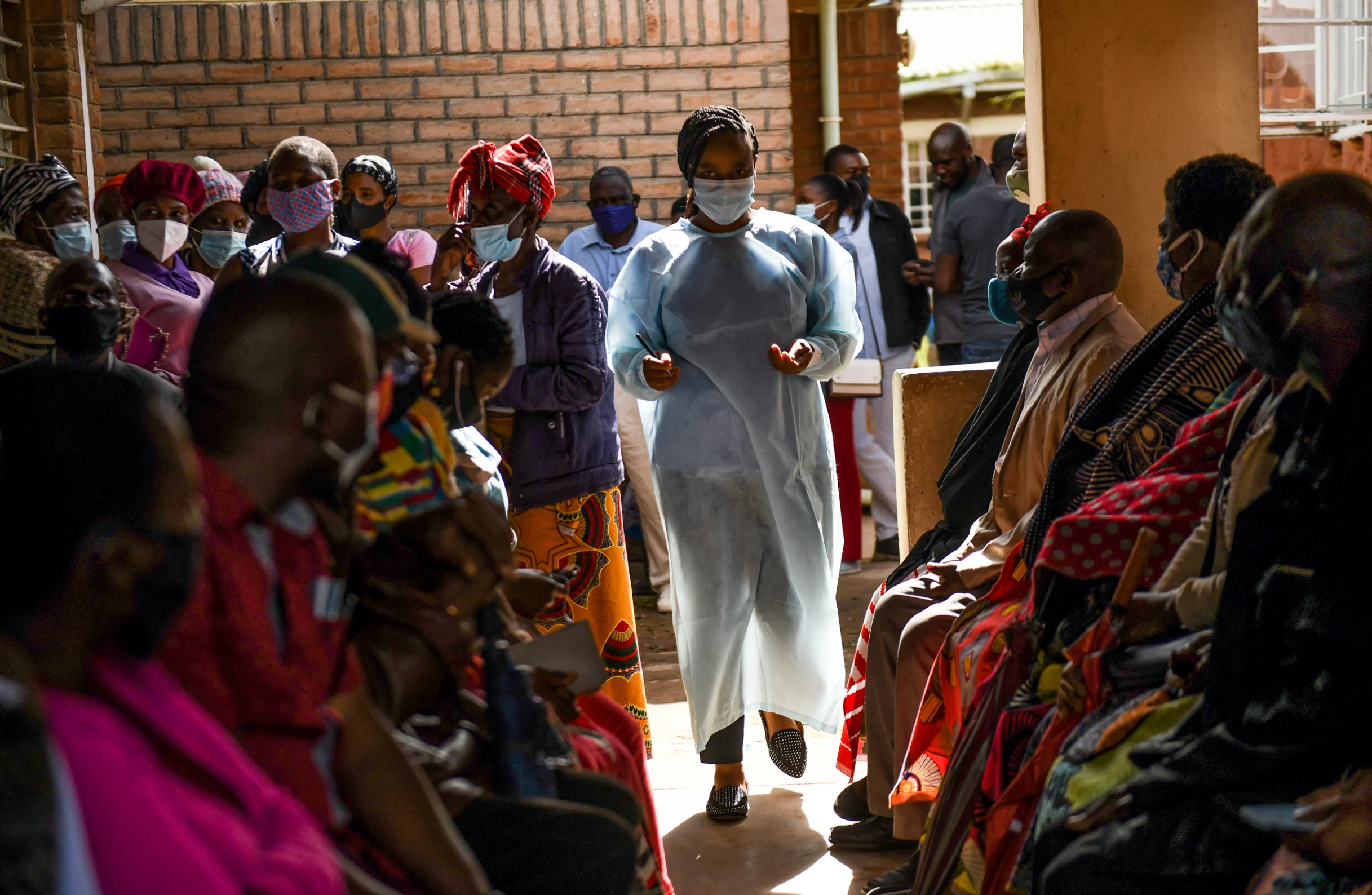 A health worker walks through a crowded clinic in Malawi. Citizens waiting for their appointments look on.