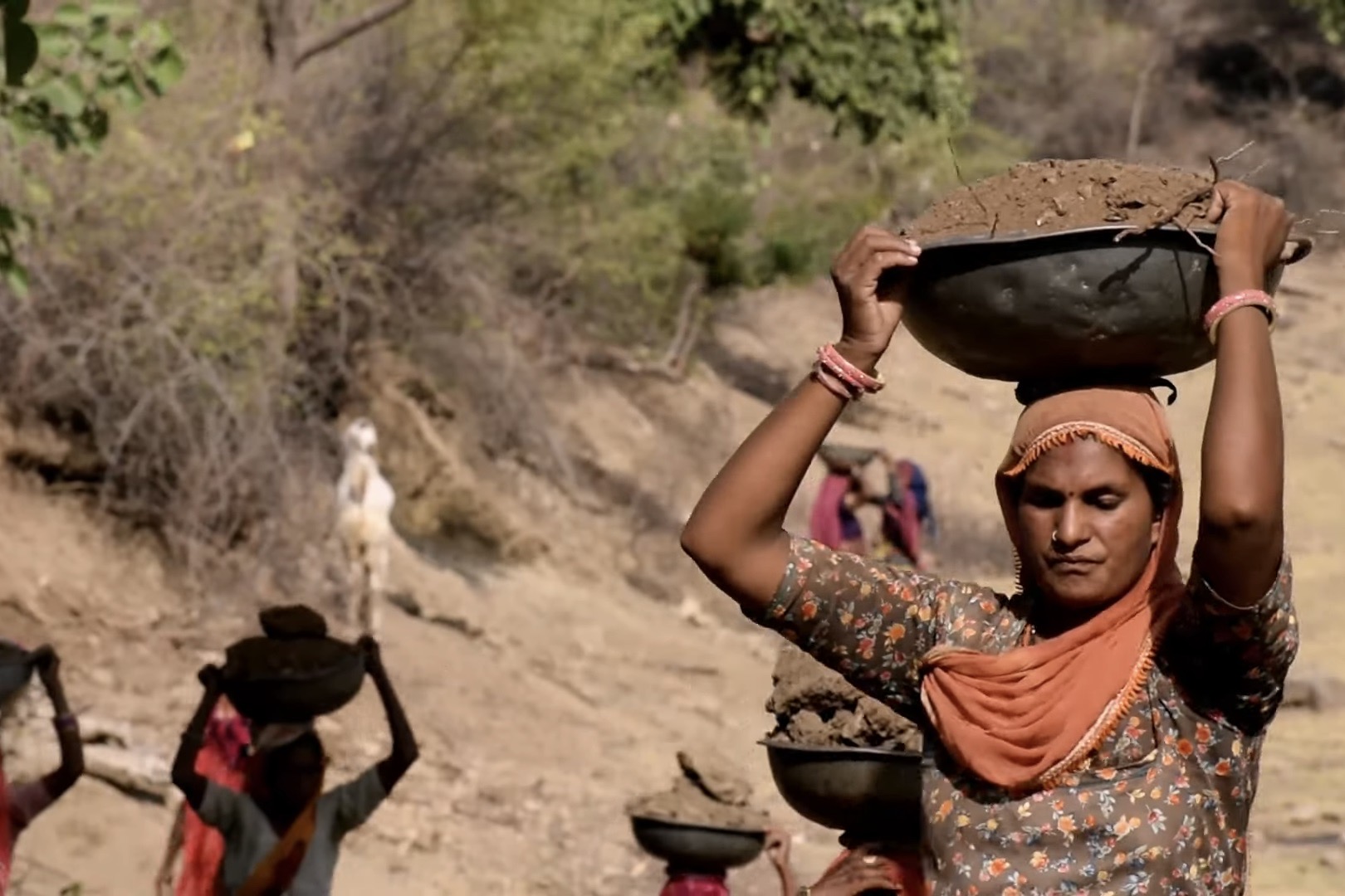 A woman laborer carries a large bowl of dirt above her head.