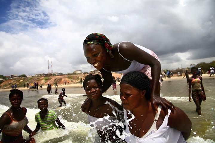 Fatima stands on the backs of other Kayayo girls while playing on a beach in Accra, October 12, 2008. She is from a village in the Northern Region, and had never seen the ocean before coming to Accra a few months prior. Coming from a predominantly Muslim society, she says she likes swimming, but doesn't like that boys and girls swim together on the beach. Image by Peter DiCampo. Ghana, 2008.